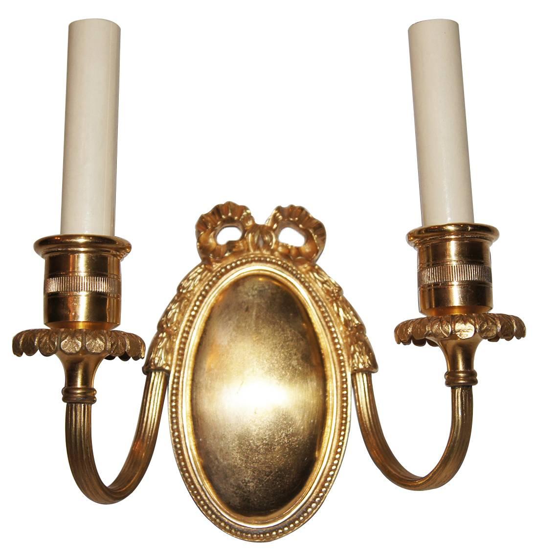 A pair of 1920s French gilt bronze, double-light sconces of neoclassic style, oval back plate, original finish.