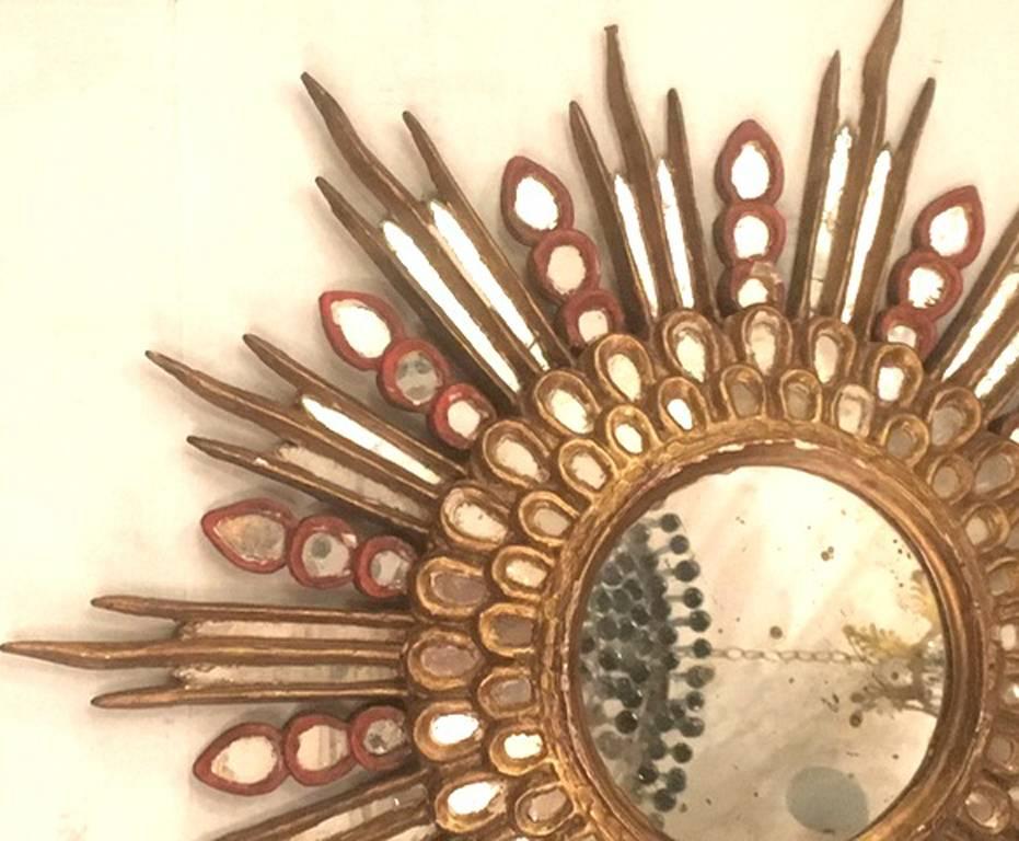 An unusual carved giltwood sunburst mirror with original red painted details.

Measurements:
Diameter 24