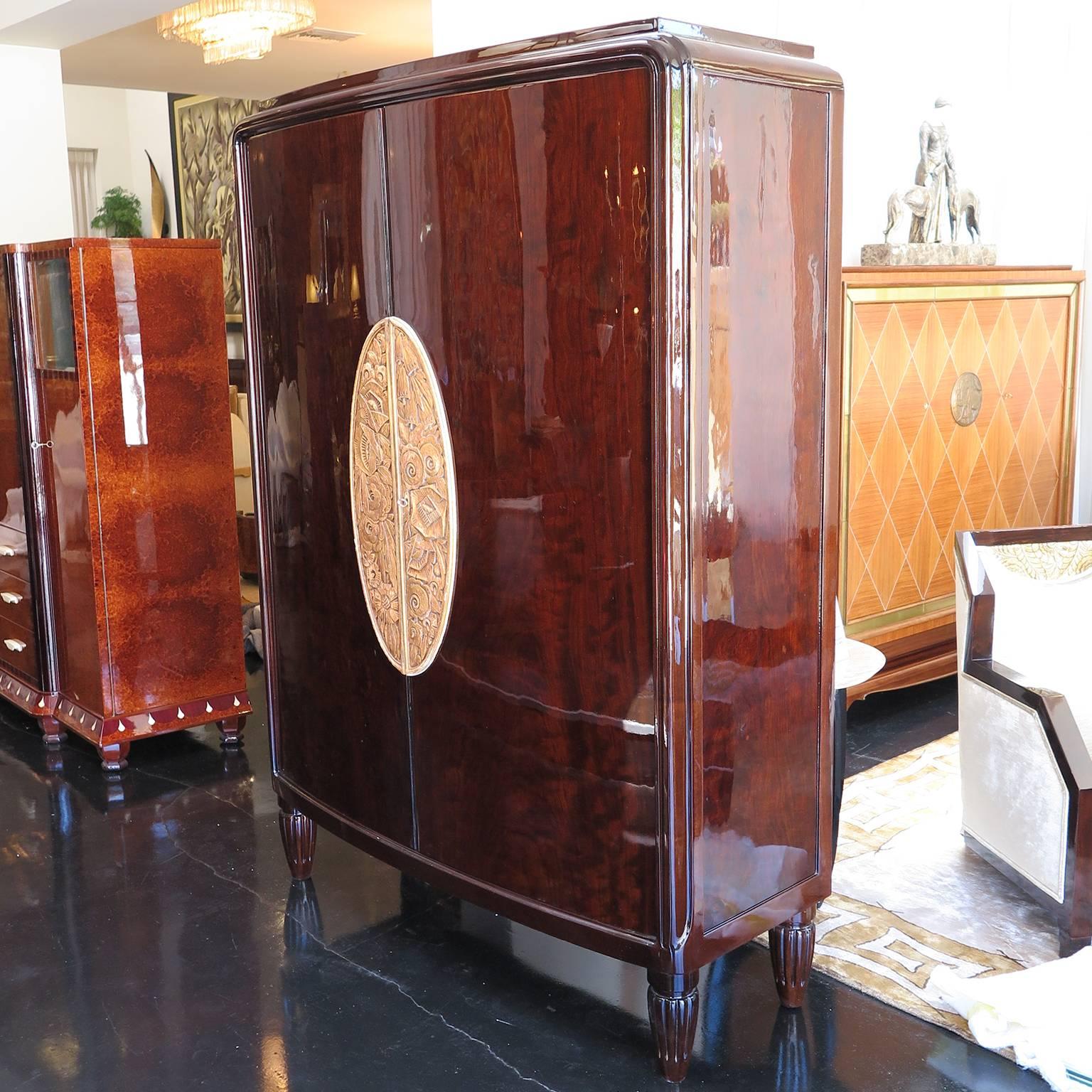 Beautiful Art Deco armoire wardrobe by Louis Majorelle. Signed Majorelle, Nancy. Dark stained oak frame and legs in high gloss finish. Four ribbed feet. Oval relief carving in centre of florals and leaves in distressed gold leaf. Two doors opening