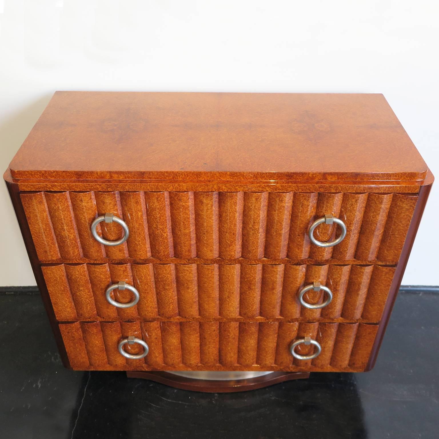 Beautiful French Art Deco dresser in exotic amboyna burl veneer with mahogany veneer on the sides. Three fluted drawers decorate the front along with six original round nickel pulls. Nickel and mahogany base.