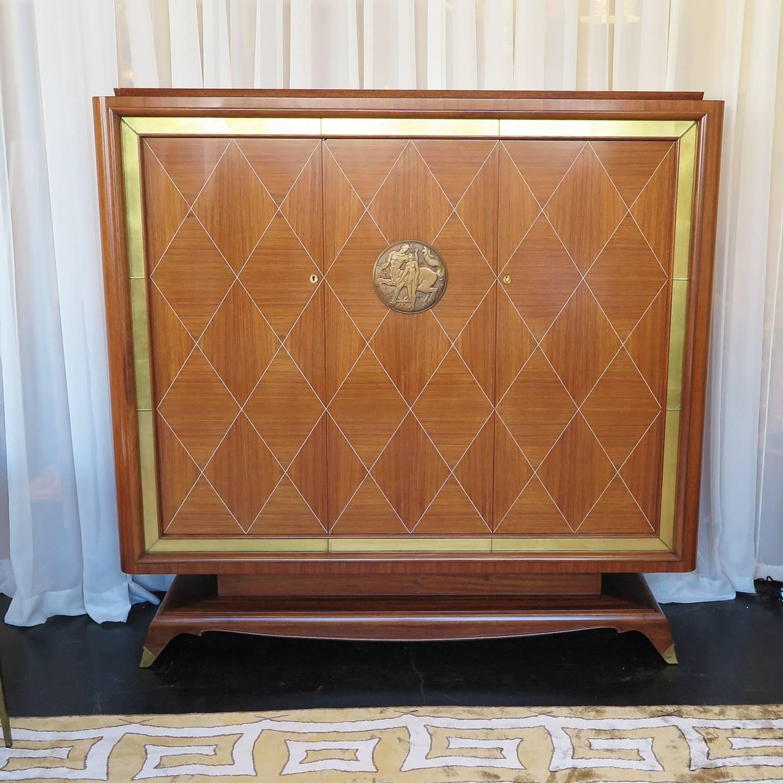 French Art Deco armoire by Jean Desnos for Rambaudi-Dantoine. Beautiful rosewood marquetry doors with criss cross inlay. Mahogany frame with gold leaf mirrored border and brass sabots. Center bronze medallion of centaur and goddess. Signature on