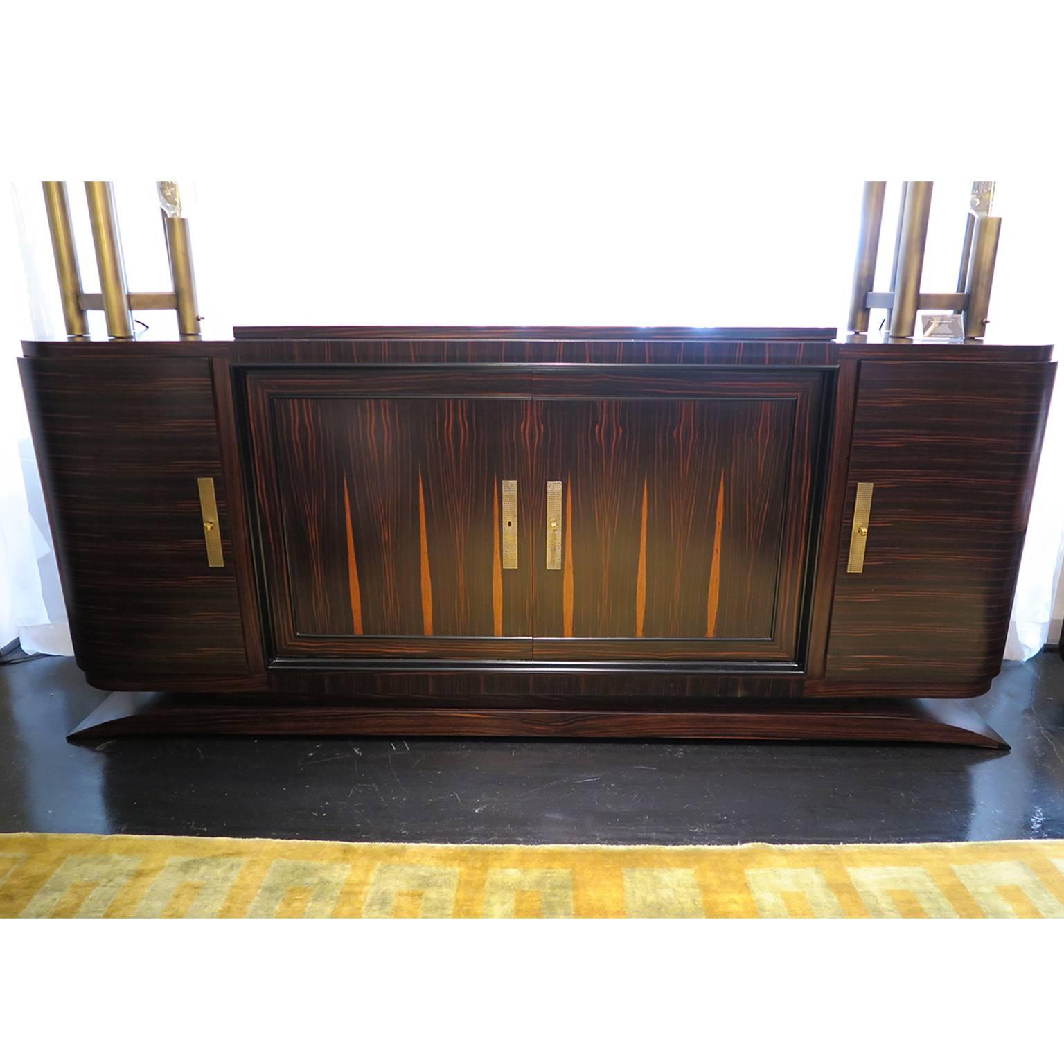 Streamline Art Deco sideboard in Macassar ebony with a matte finish. Custom textured brass rectangular hardware. Center doors open to two drawers and shelf while outside doors open to additional shelving.
