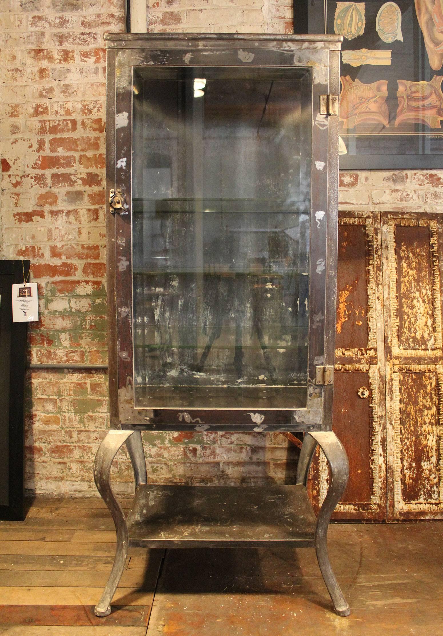 Antique metal and glass doctor's / medical cabinet with cabriole legs and 3 5/16 glass shelves. Vintage steel / glass / cast iron storage cabinet is from the 1920s. All original. In great condition minus a few chips to the glass shelves. Cabinet