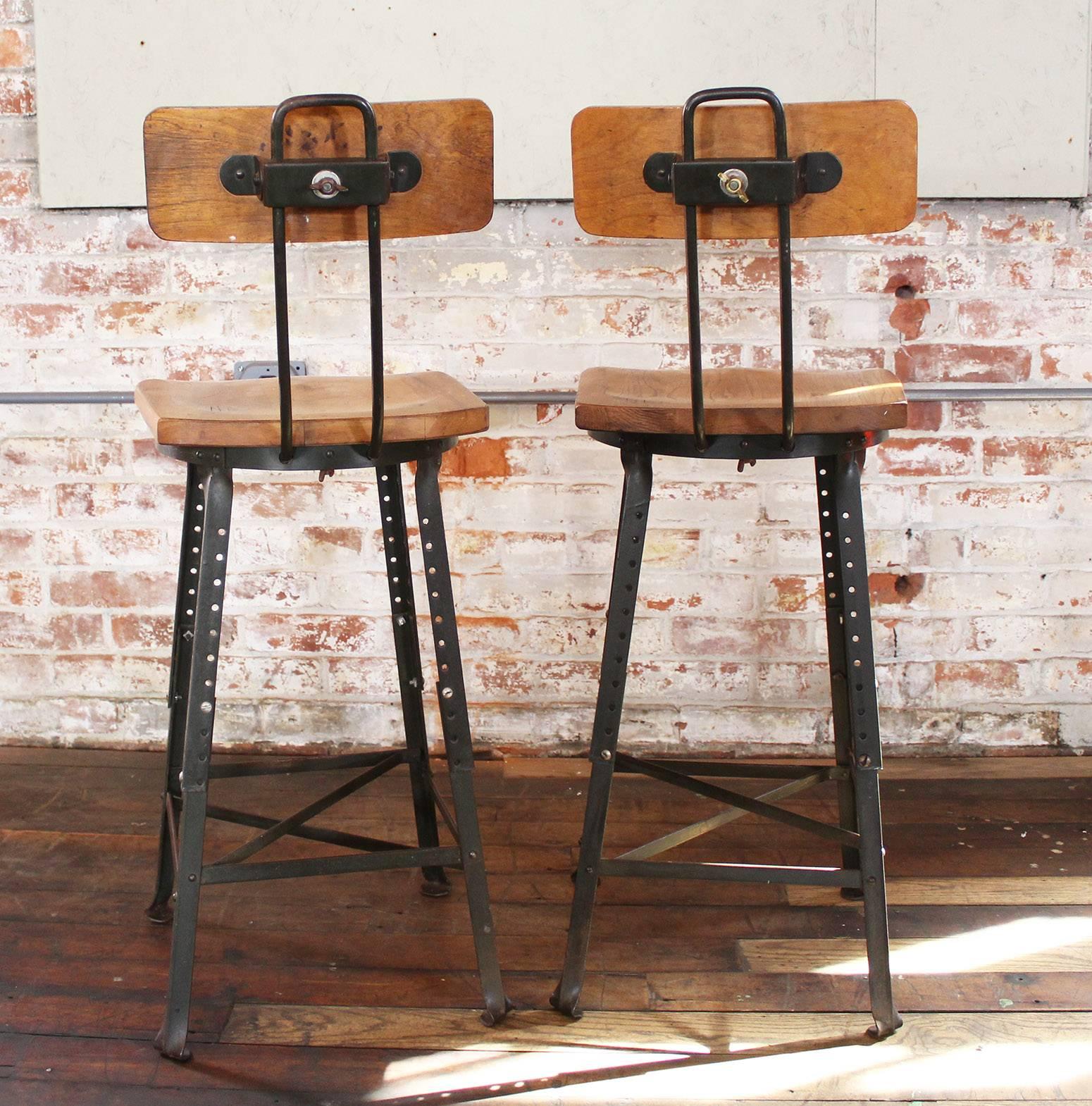 Pair of vintage Industrial adjustable wood and metal factory shop bar stools. Great condition, adjustable seat height and seat backs. Overall dimensions are set at 38" in height, 15 1/4" in width and 19" in depth. Seat measures 14