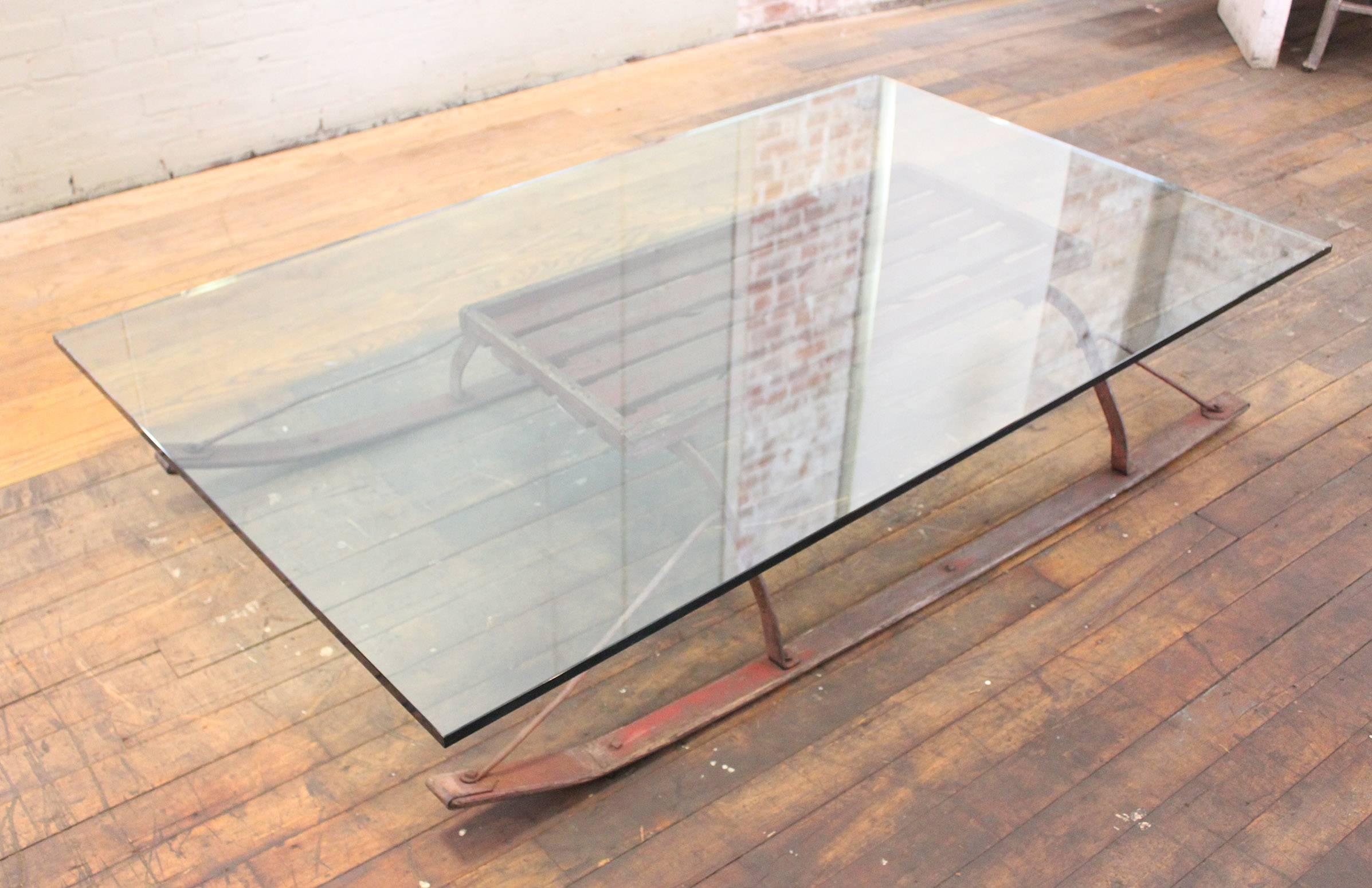Un traîneau vintage en bois et en acier transformé en table basse avec un plateau en verre. Le traîneau mesure 67 1/2