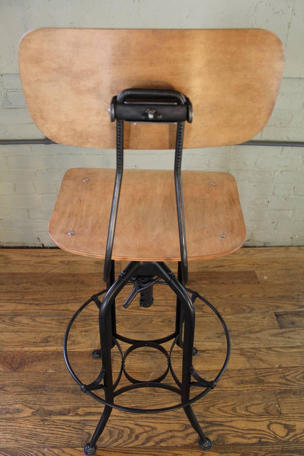 Vintage Industrial bent plywood and metal adjustable toledo bar stool, overall height ranges from 42"-47", seat height ranges from 28"-33". Footrest diameter measures 18 1/8", and sits 13" in height.