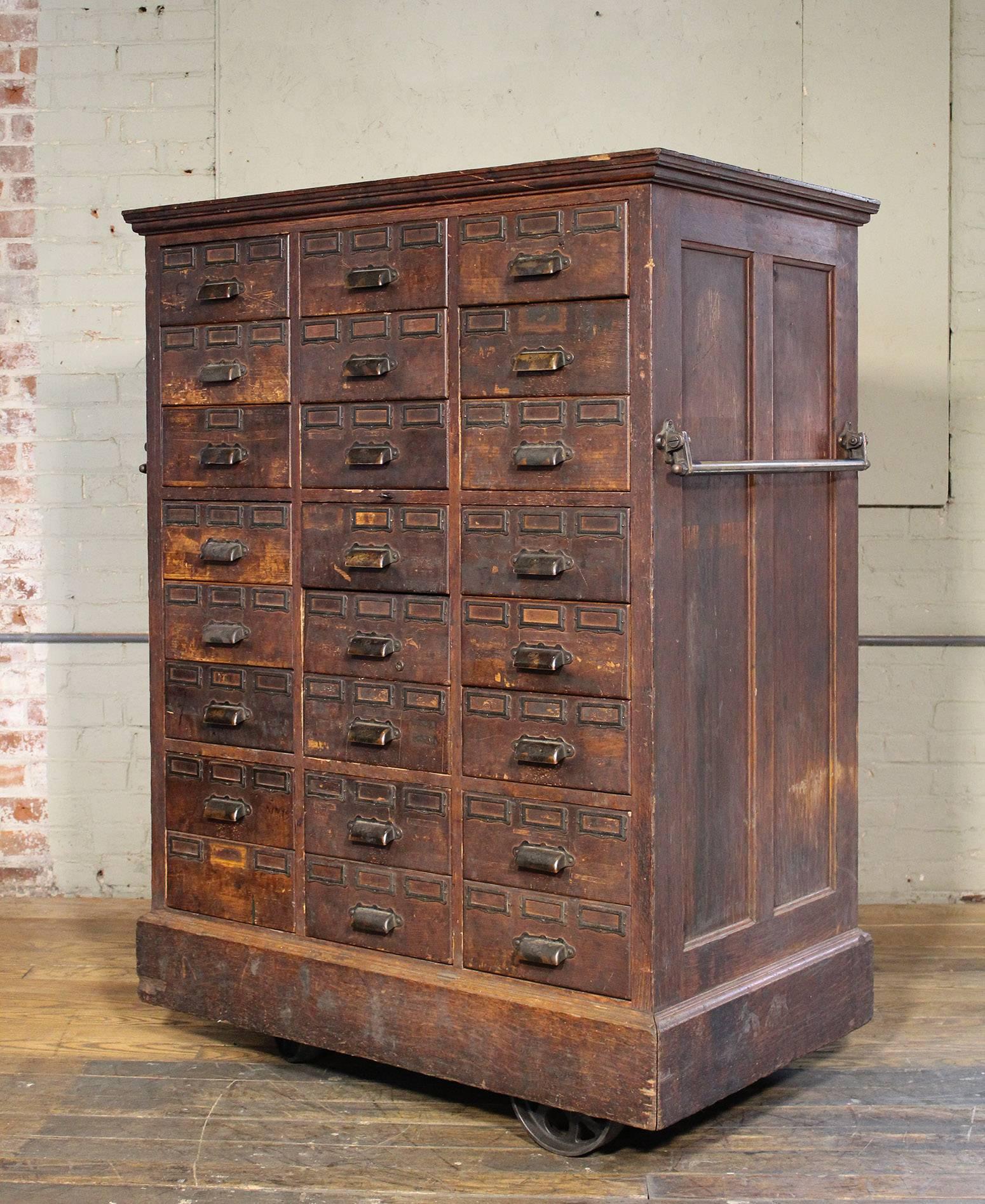 Rolling distressed apothecary wood storage cabinet, vintage Industrial with brass hardware. Lower six drawers are double drawers. Cabinet is on four cast iron wheels, two are swivel. Overall dimensions measure 40 1/2" x 25 1/2" x 53