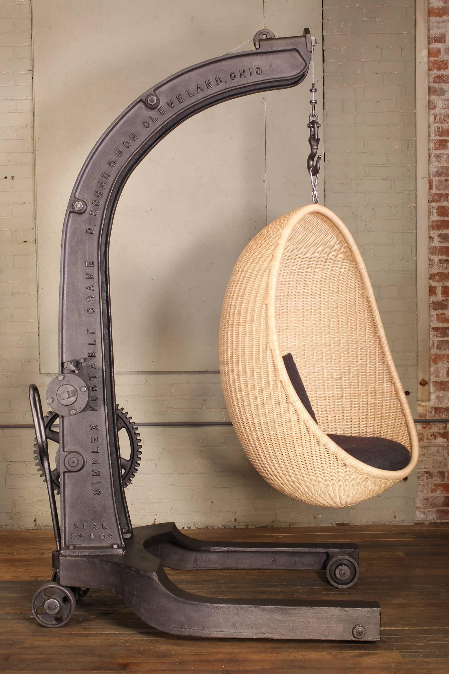 Authentic 1920s cast iron manual crank engine hoist. Combined with a woven rattan Nanna Ditzel hanging interior egg chair in natural, with charcoal cushion. Seat height is adjustable by engaging the crank mechanism handle. Rear casters remain locked