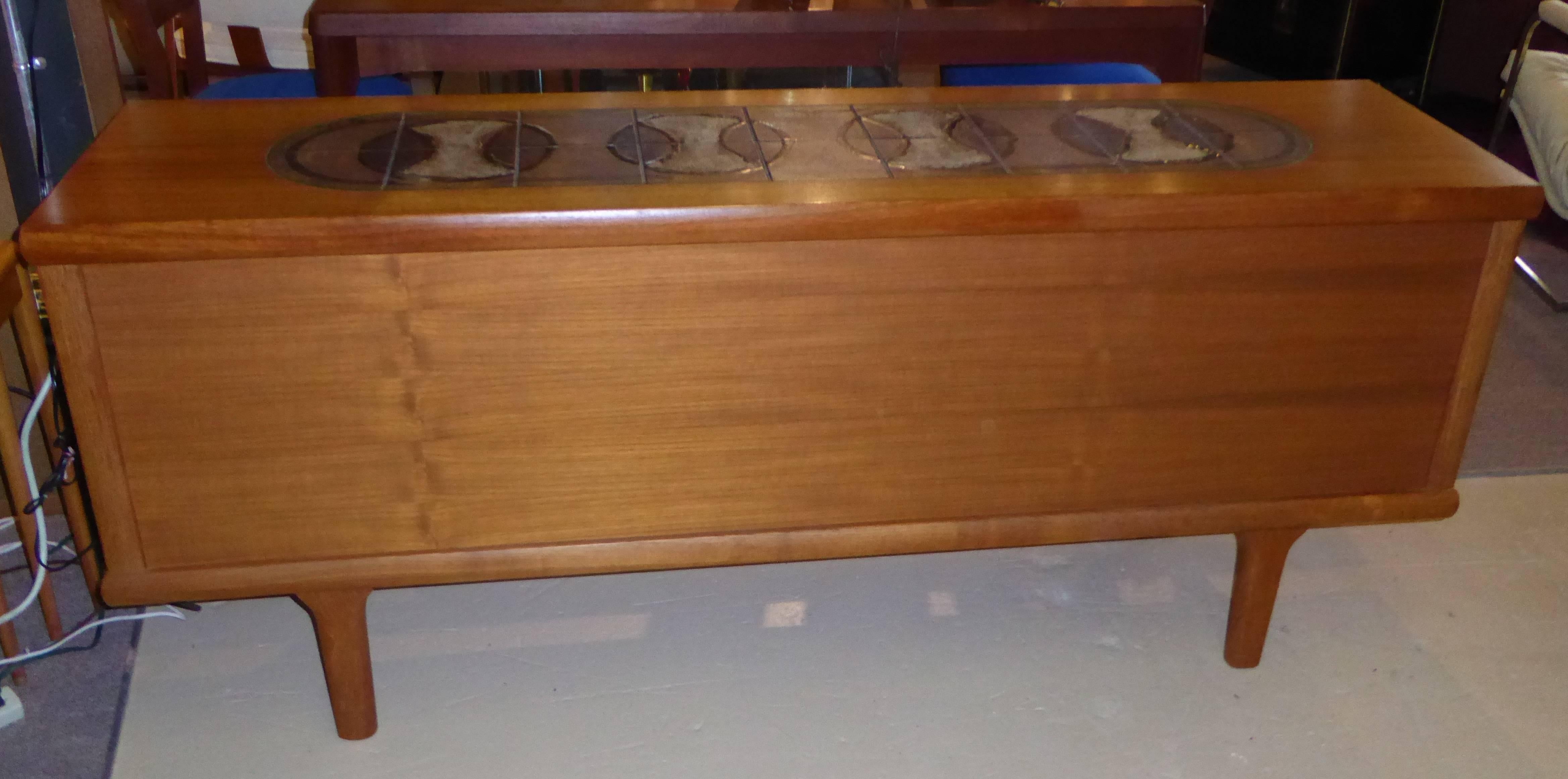 1960s Danish teak sideboard Credenza with inset signed tile top featuring three center drawers, the top drawer felt lined and sliding doors left and right opening to shelved interior storage.
In very good original condition with some scratches