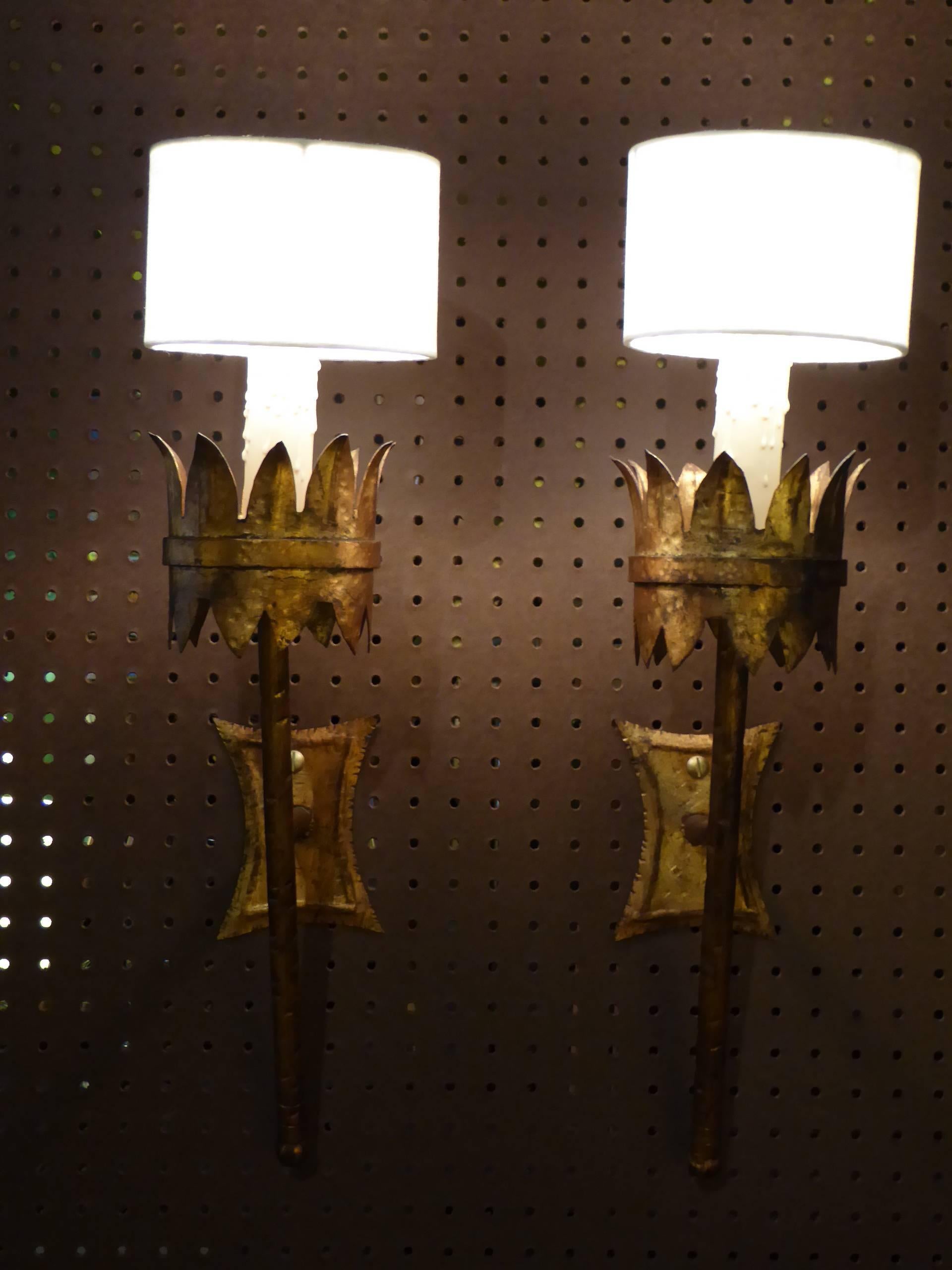 Regal and elegant, this pair of 1950s Gothic style Sconces with a wall torch design is gilt tole and iron. Newly rewired and with new UL medium base sockets, they have faux wax candle covers and new pill box linen shades.
Shaped backplate with