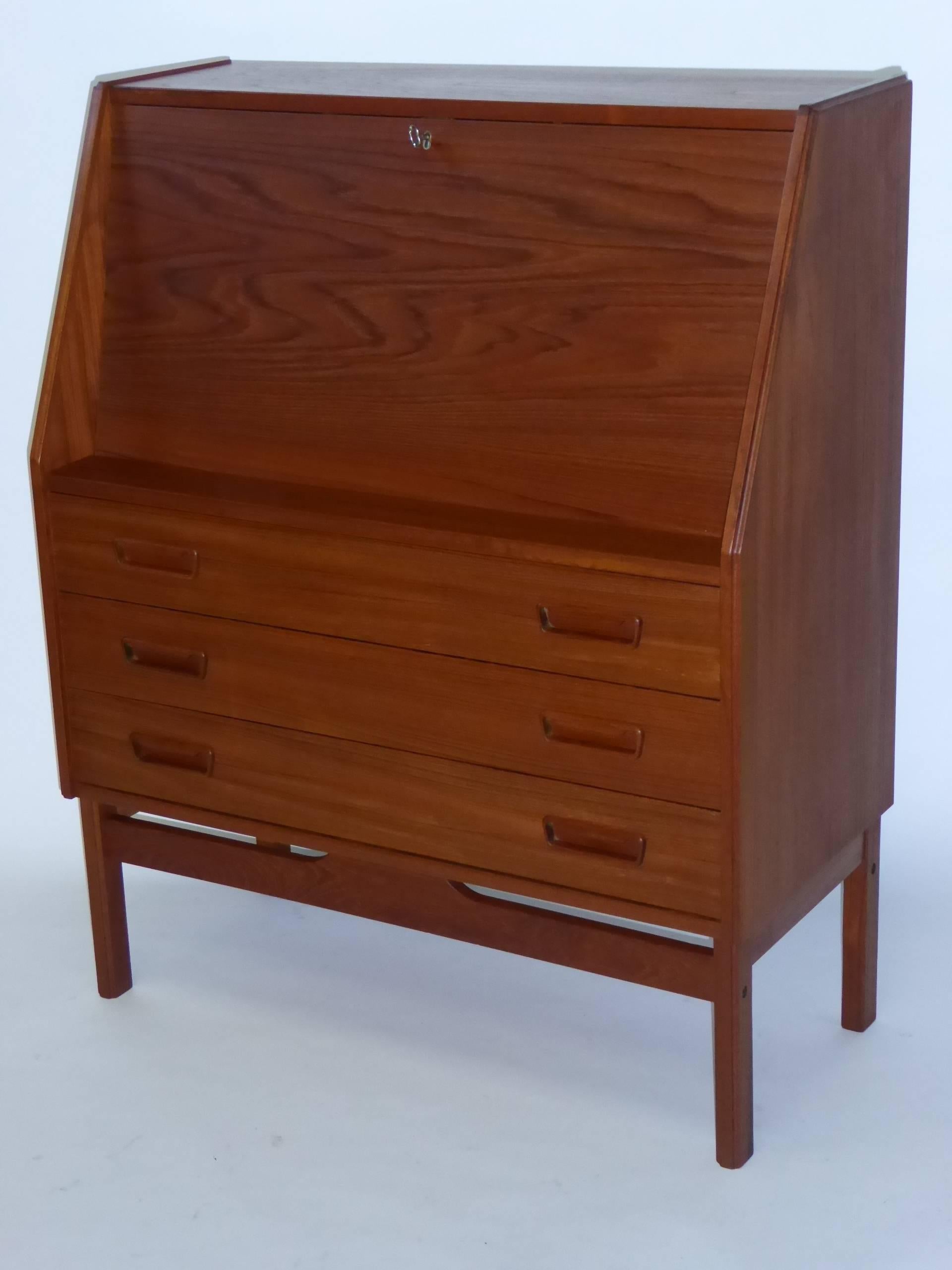 ...SOLD...Late 1960s Dyrlund Danish teak drop front secretary with three bottom drawers. With original key, the drop front opens to a fitted interior of small drawers and slotted shelf. Beautiful warm teak, beautifully figured, carved drawer pulls,