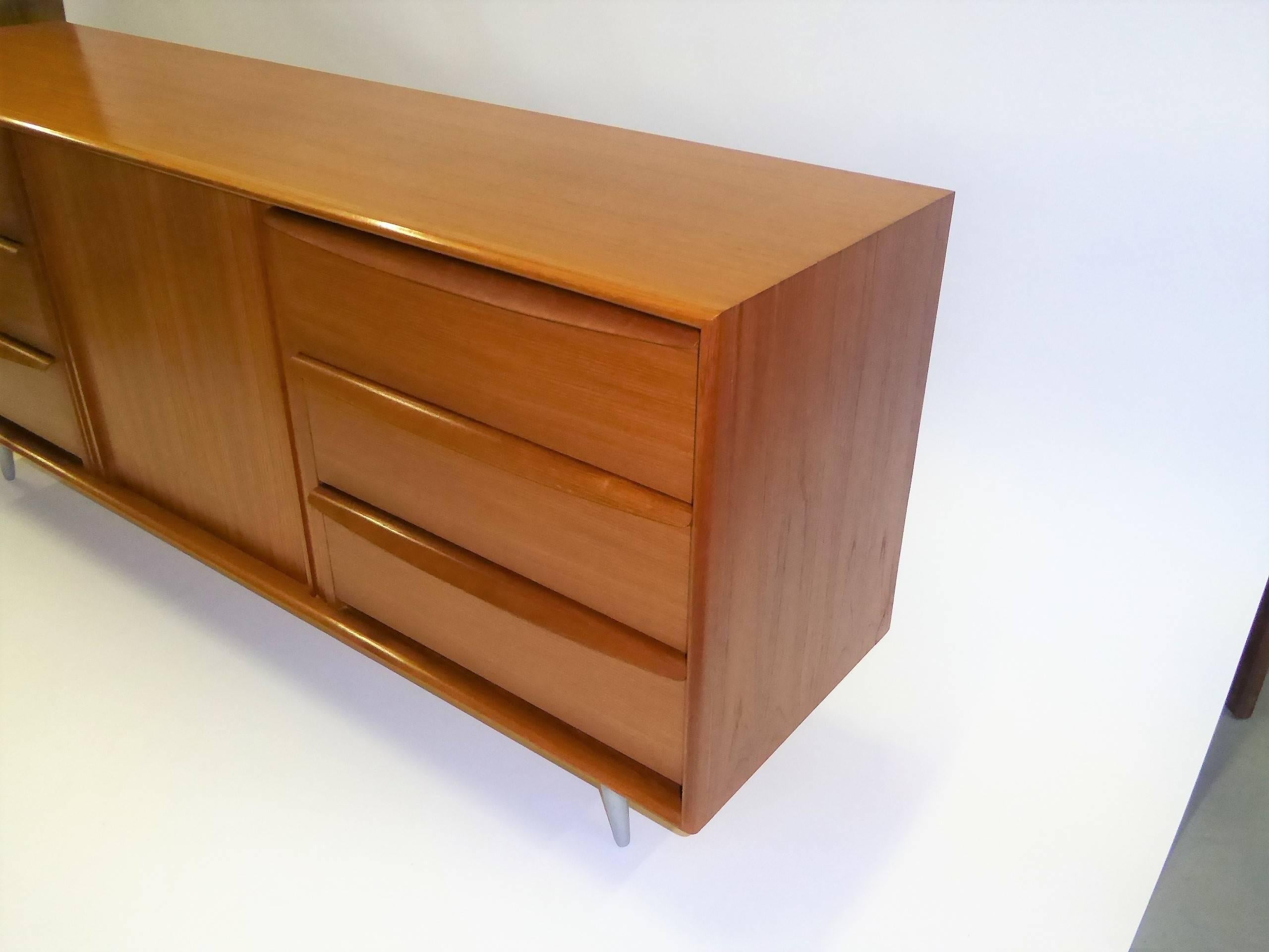 Very fine, 1970 Danish teak sideboard Credenza by Danflex Systems with six drawers and an adjustable shelf behind a centered tambour sliding door. Beautiful curved handles and molded edges and unique tapered legs in a matte finish aluminum.
Marked