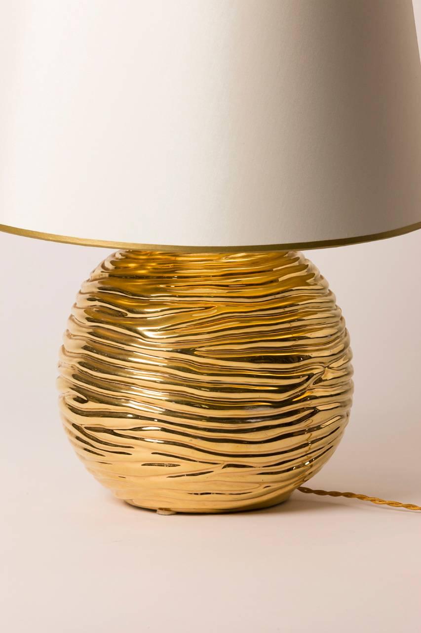 Mid-Century Modern French table lamp. Lamp is ceramic and features bright gold glaze which accents the ripple motif. Custom silk shade with gilt lining created in Paris.