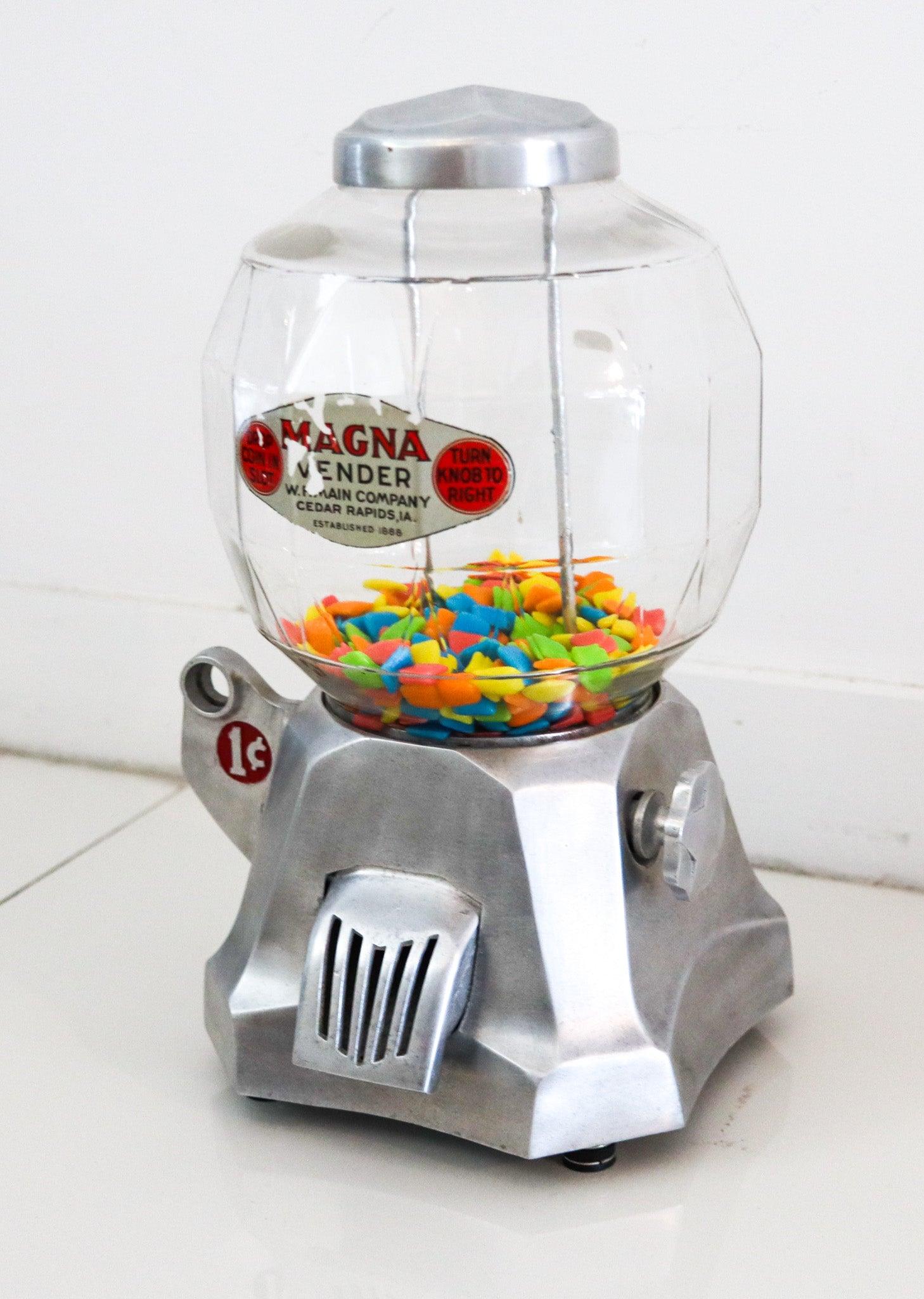 Un distributore automatico di caramelle da banco di Machin.

Si tratta di un'antica macchina per noccioline Magna Vendor. Il distributore automatico è stato realizzato negli Stati Uniti, in Iowa, dalla National Manufacturing Co. nel 1934. Progettato