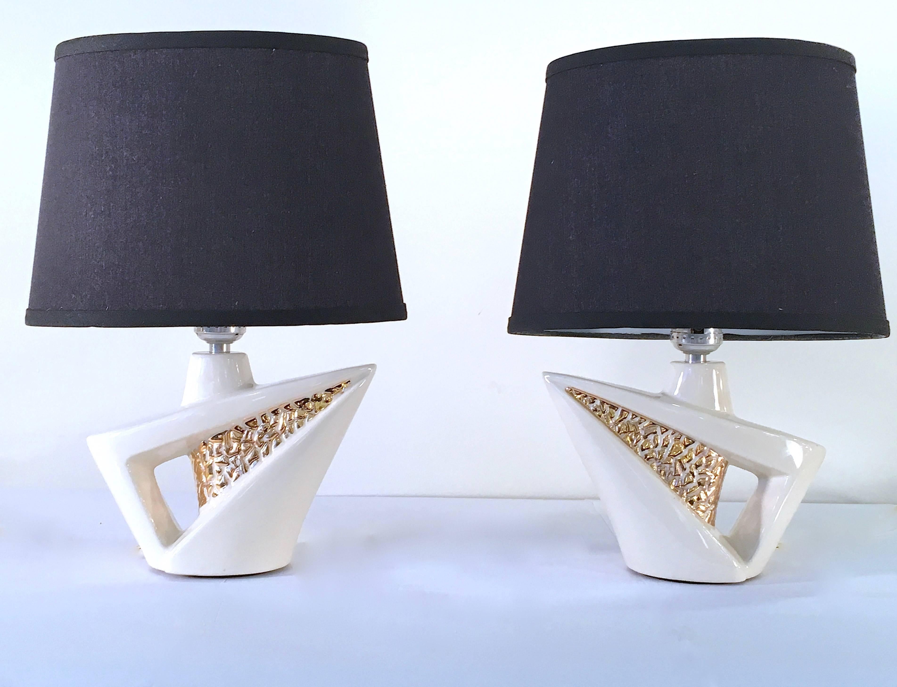 Charming pair of sculptural modernist lamps in a small, versatile scale. The lamps are ceramic in a cream colored glaze with gold accenting. Please contact for location. 