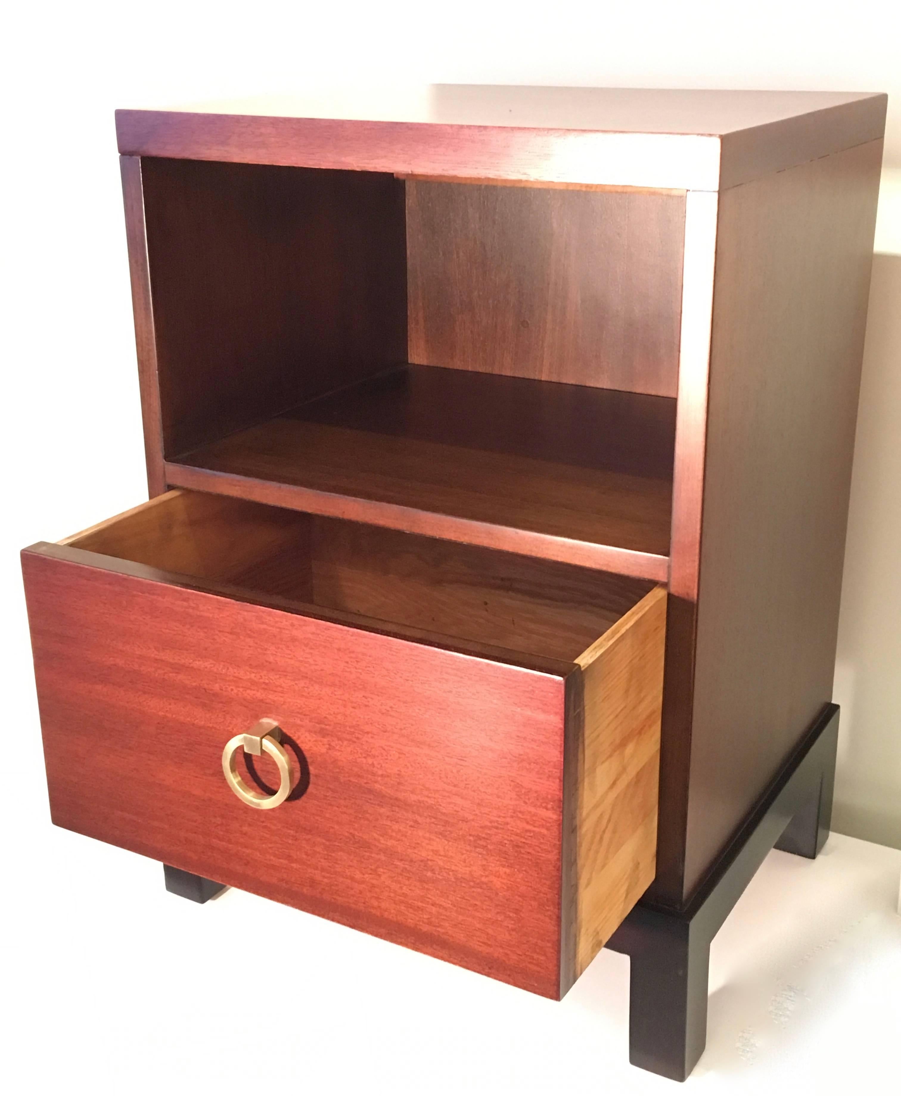 A very handsome and stately pair of nightstands or end tables refinished in a rich walnut stain. The cabinets are supported on plinths that have been lacquered in espresso and each stand is accented with Robsjohn-Gibbings' signature polished brass
