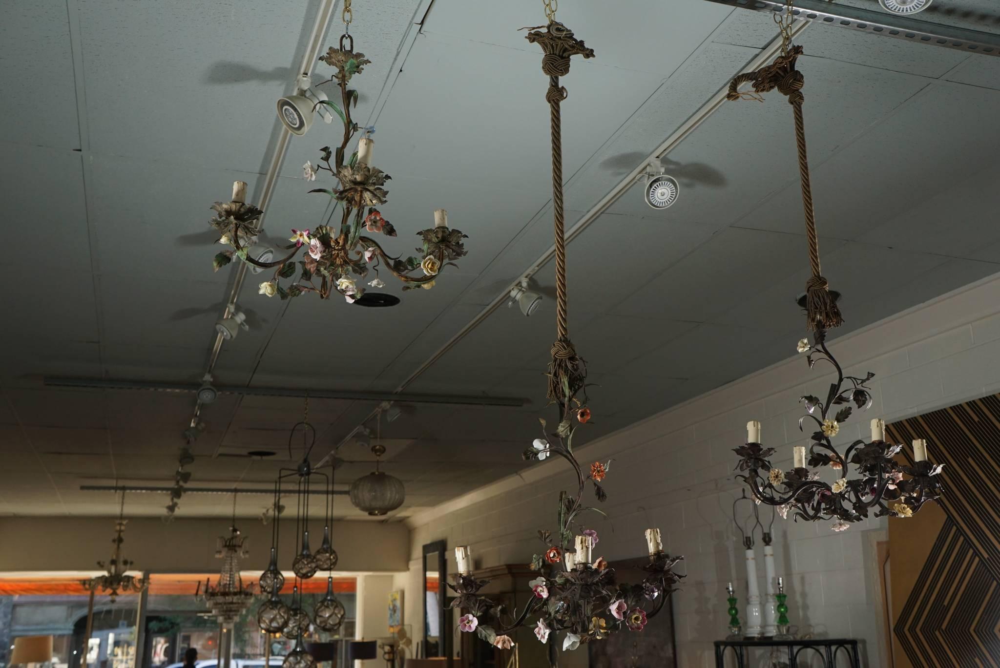Here is a set of three tole flower bouquet petit chandeliers. The chandeliers look great as a cluster of three. Two of the chandeliers have vintage gold toned cords and tassels. These pieces are available as a group or as singles for $950. Each. The