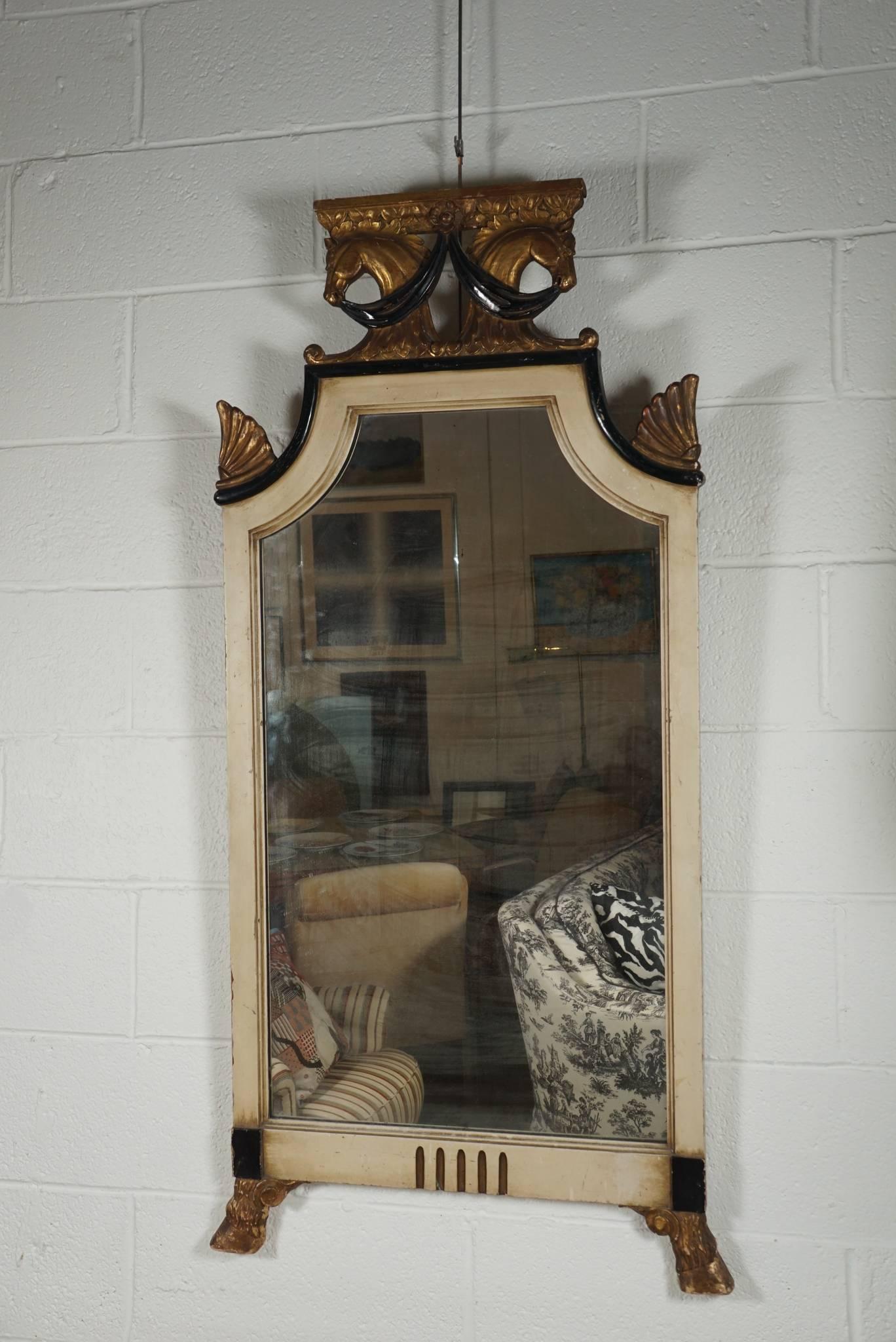 Here is a great Regency style mirror with a unique double horse head finial. The horse head motif is reflected in the footed hooves base.
The mirror is painted while the ornamented features are gilded.