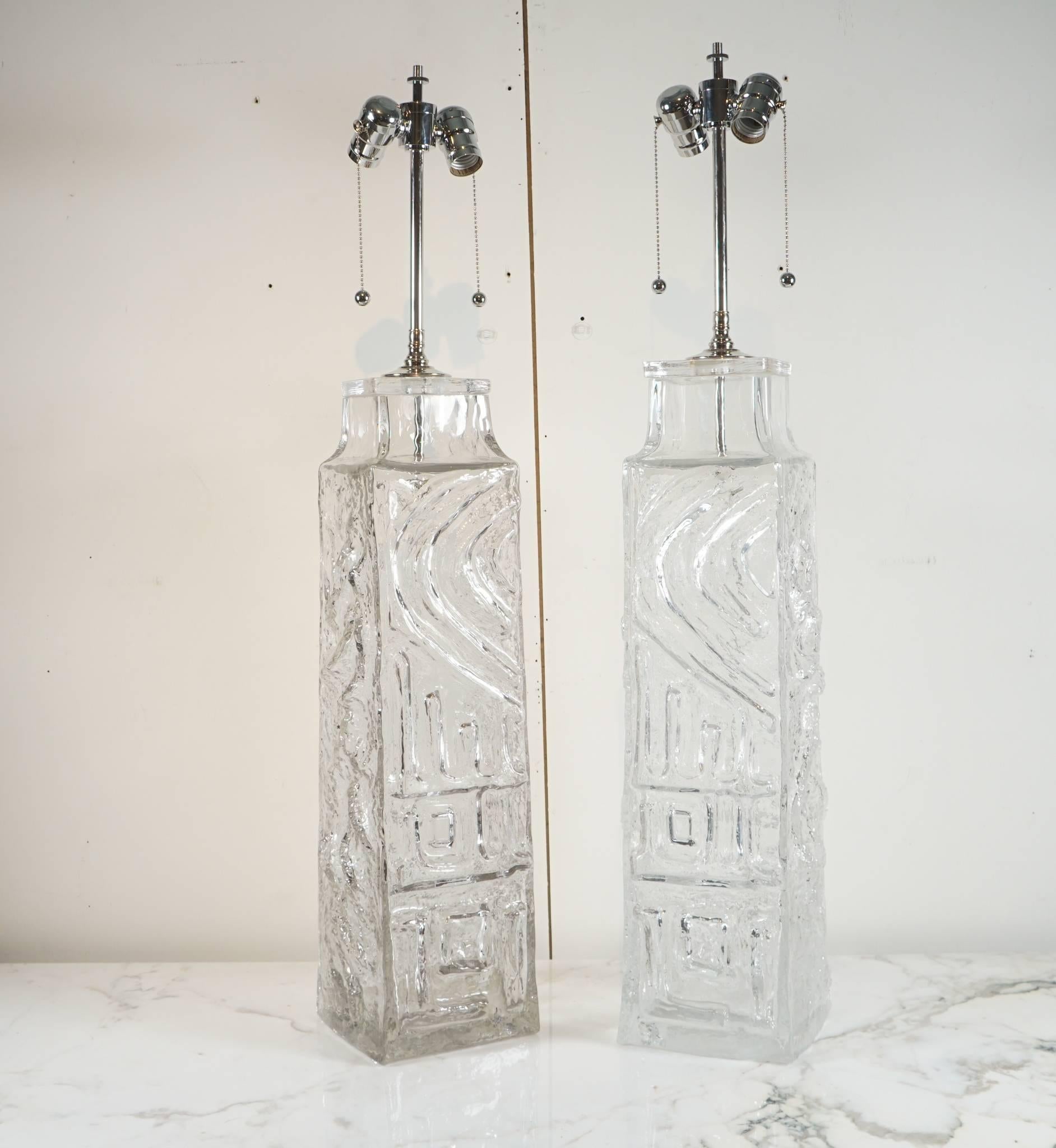 Here is a monumental pair of Geoffrey Baxter glass lamps for the Whitefriars Company. In his signature style, the lamps have a textured pattern and the glass is clear as ice. The lamps have all new chrome hardware and double sockets. The lamps are