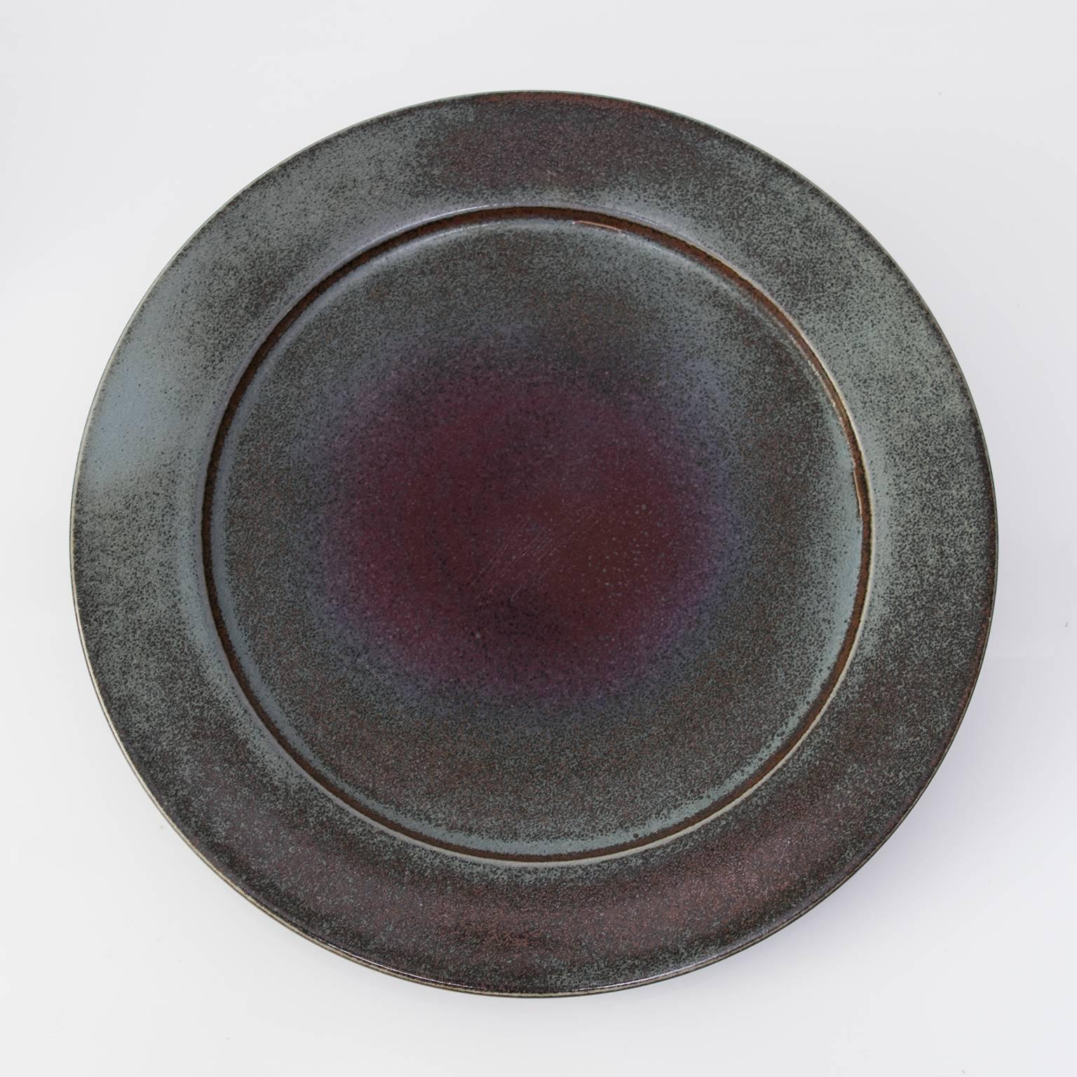 A large unique studio piece by Swedish ceramists Stig Lindberg. This piece is masterfully thrown and glazed with rich to subtle color shifts. This ceramic charger has a low profile and a recessed foot which gives it a hovering effect. Signed on the