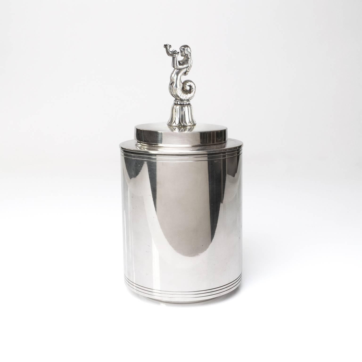 Scandinavian Modern silver plated lidded jar by C.G. Hallberg, Stockholm, Sweden. The lid feature a mermaid figure holding a baby dolphin. A very clean Minimalist design with engraved bands across the base and just below the lid. 
Measures: Height