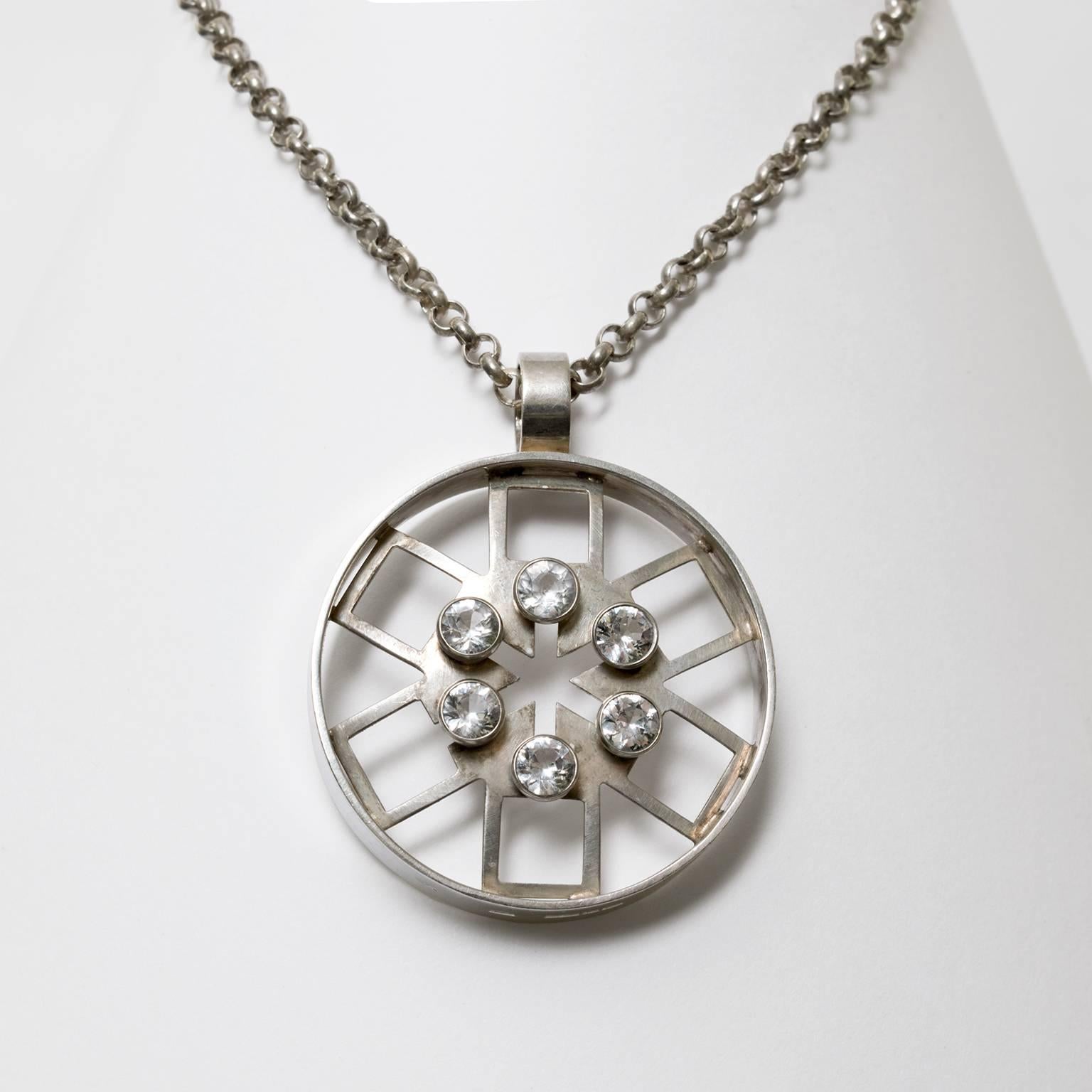 A silver Scandinavian Modern pendant and chain with a geometric hexagonal design within a circle and detailed with six rock crystals. Made by Kultateollisuus KY Turku, Finland, 1972.
Diameter: 2".
Chain length: 28".