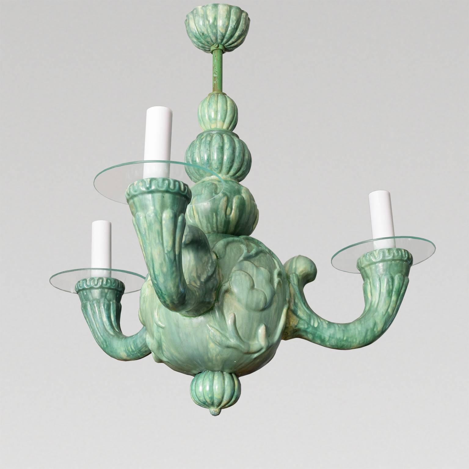 A Swedish Art Deco, Scandinavian Modern glazed ceramic chandelier with three-arms each with a standard Edison base socket within a candle sleeve atop a clear glass bobeche. The center globe has stylized flowers and leaves. The fixture has been