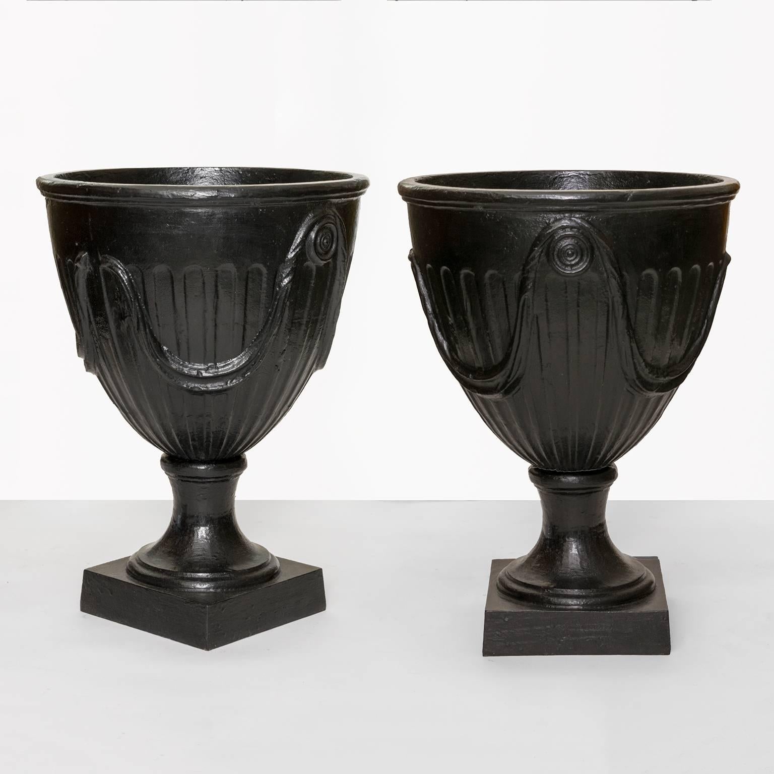 A large pair of Swedish Art Deco cast iron urns with a relief of draped fabric over a pair of rosettes. The bodies' are fluted and rest on a square plinths. Designed in the 1930s this pair is later production, designer unknown.
 
Measure: Height