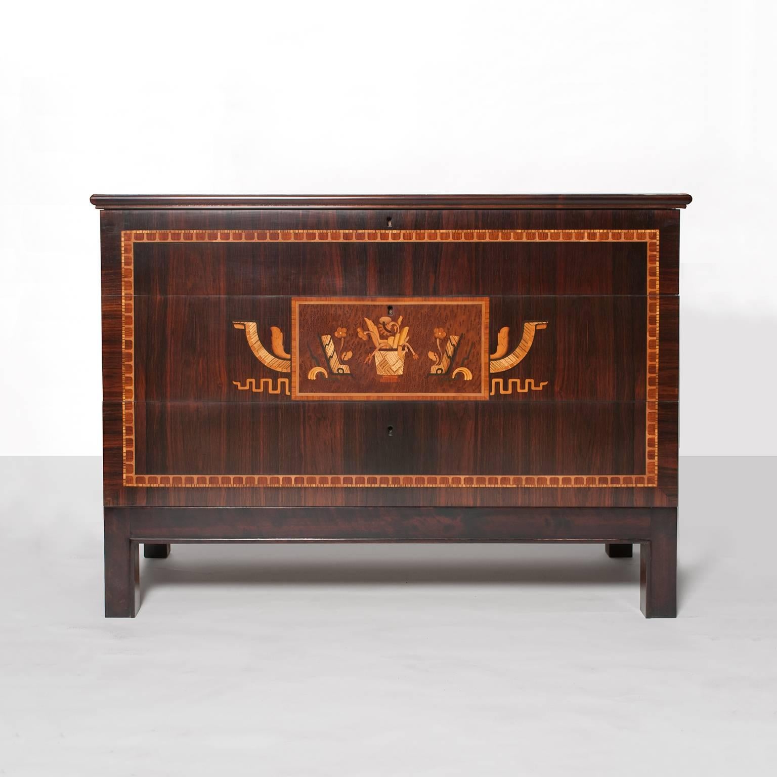 Swedish Art Deco chest with 3 drawers. Veneered in rosewood and finely detailed with bands of marquetry on the front, sides and top. The center drawer has a beautiful marquetry cartouche depicting stylized flowers in a basket with flanking abstract
