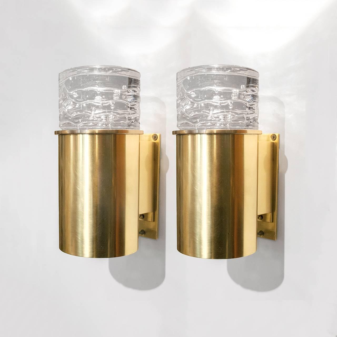 Pair of Scandinavian Modern midcentury polished brass sconces with a cylindrical form topped with a heavy crystal glass element. Each sconce is supported by an arm which mounts onto a sliding wall plate. Newly rewired with a single candelabra bulb