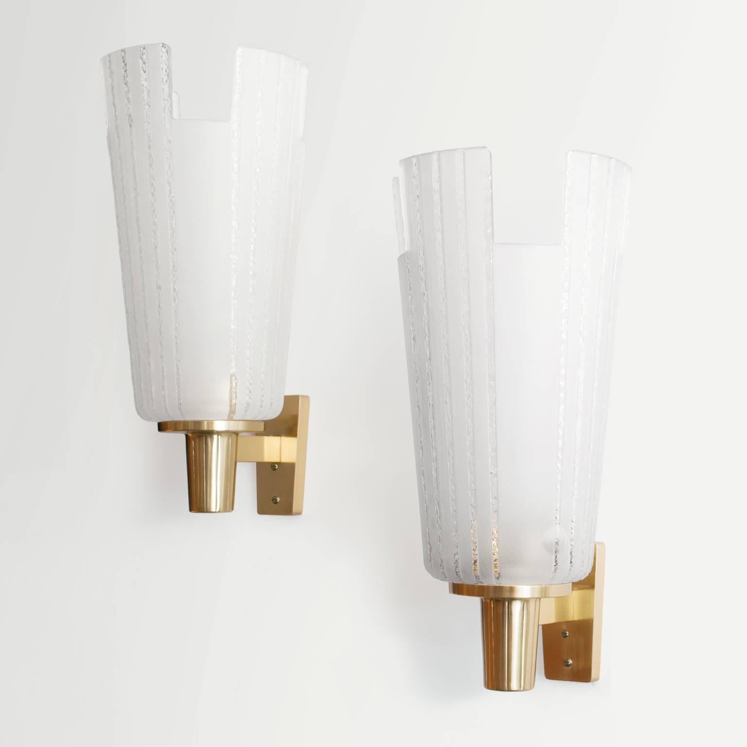 Large pair of Scandinavian Modern single-arm sconces made by Orrefors. Each sconce has a hand and acid etched glass shade with notched sections along the top. Polished brass arms extend from and easily mounted wall plaque. Impressive in scale and
