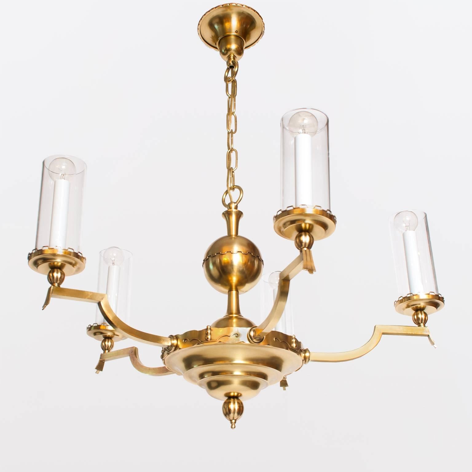 Scandinavian Modern, Swedish art deco five-arm chandelier in polished brass made circa late 1920s. Each arm is detailed with a stylized drape, a reeded sphere, a stepped bobeche and a candelabra base sleeve surround by a glass cylinder shade. The