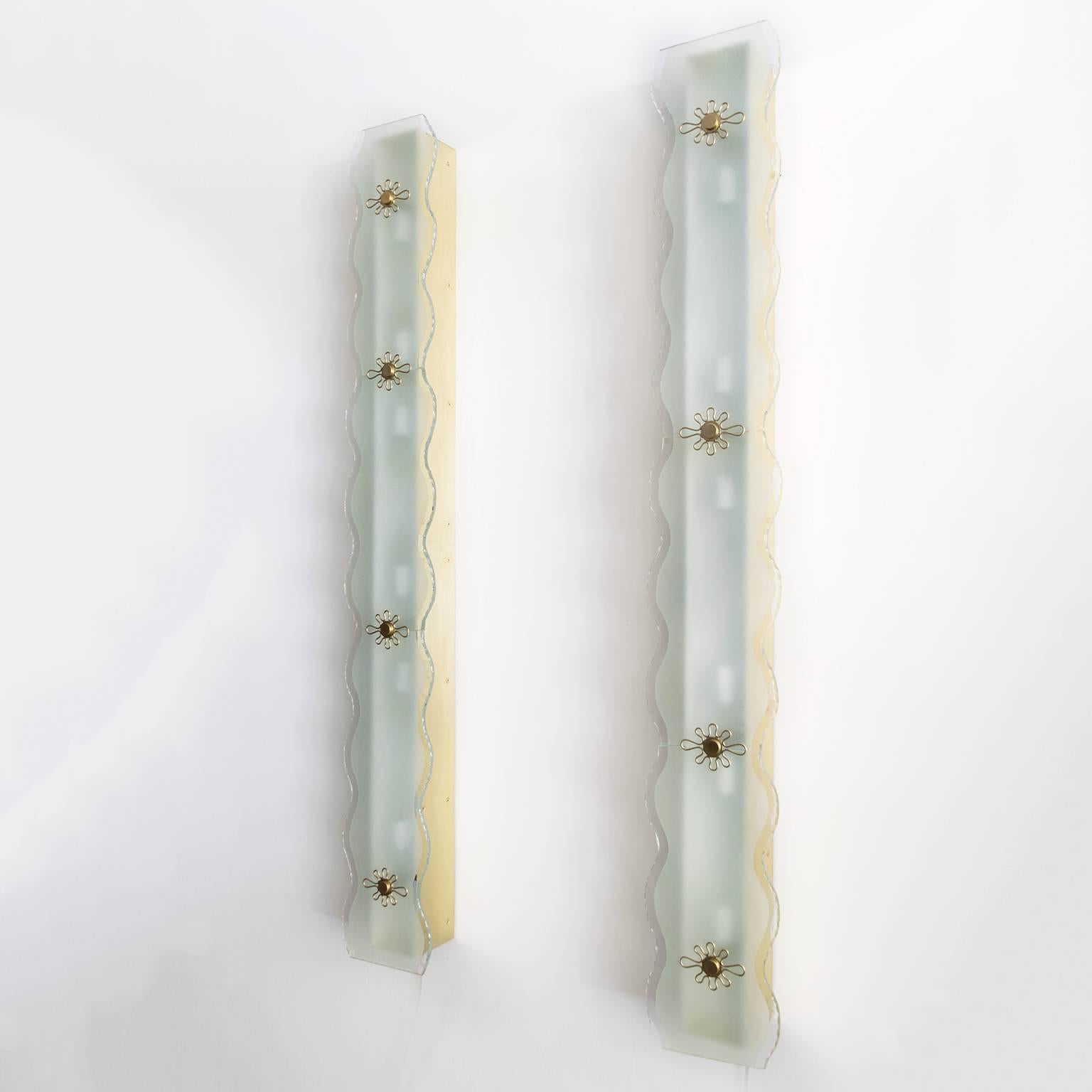 One of two large pairs of Scandinavian Modern wall lamps / flush mount fixtures veneered with brass panels. Each lamp has textured glass plates with scalloped edges and partial frosted areas. Decorative polished solid brass details hold glass in