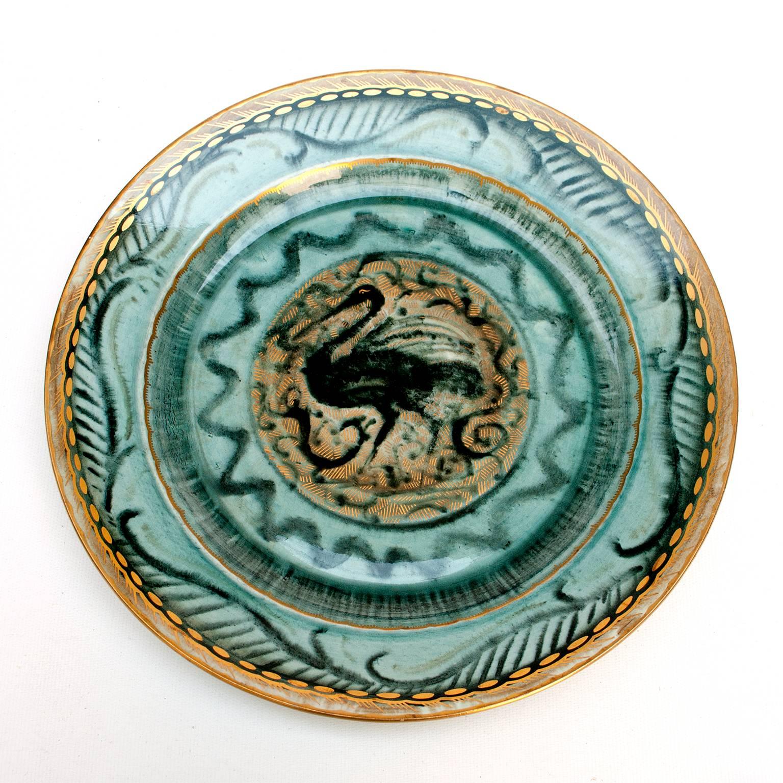 A large beautiful Swedish Art Deco hand decorated ceramic charger designed by Josef Ekberg for Gustavsberg. A rendering of a black crane at the center fills the center and is surrounded by a luster glaze in a blue-green with details in gold. Signed