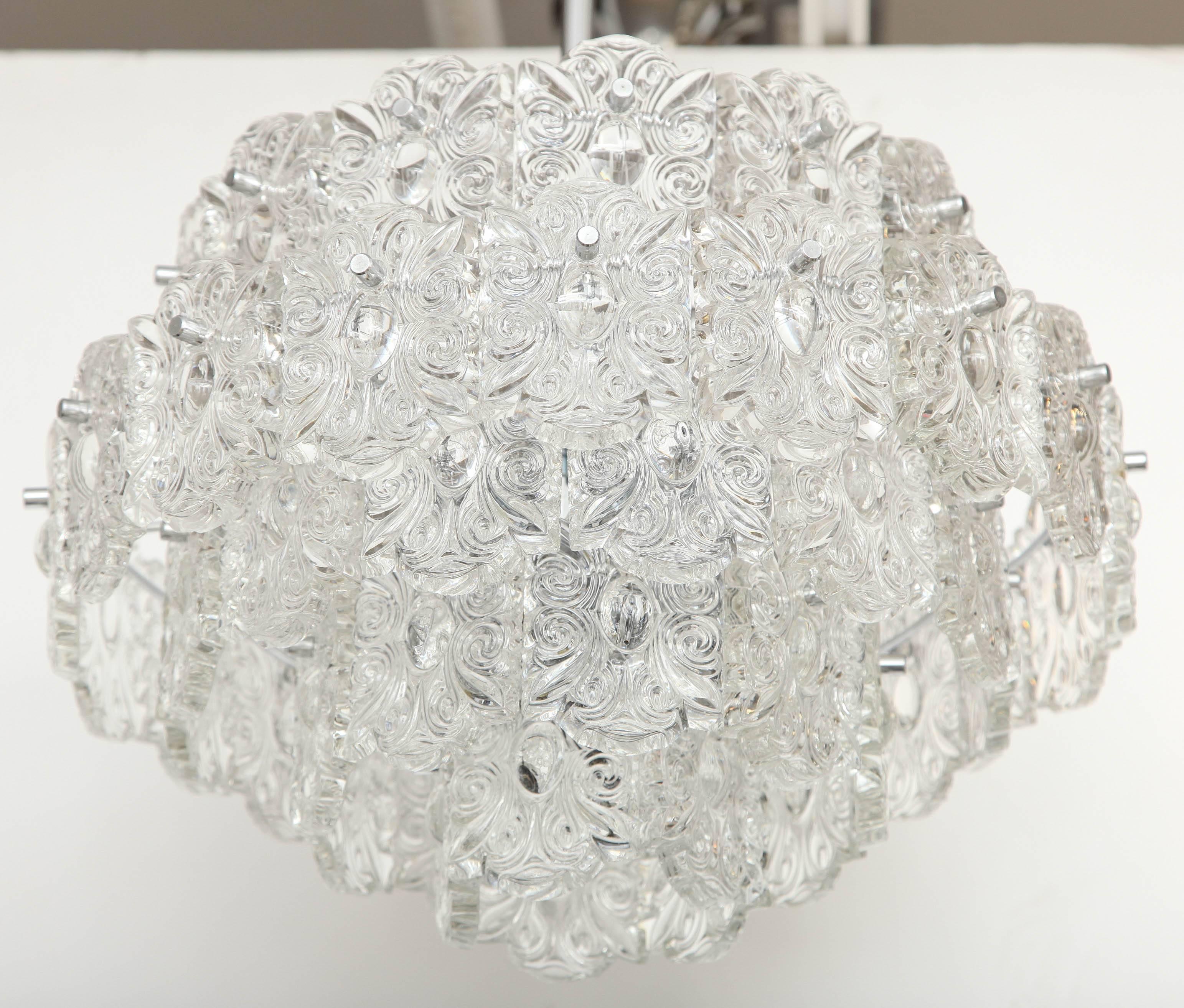 Striking midcentury chandelier composed of five tiers of crystal elements with a scroll design. Chandelier suspended from a nickel canopy and rod. Rewired for use in the USA. 12 sockets using candelabra type bulbs.

Measures: Chandelier body