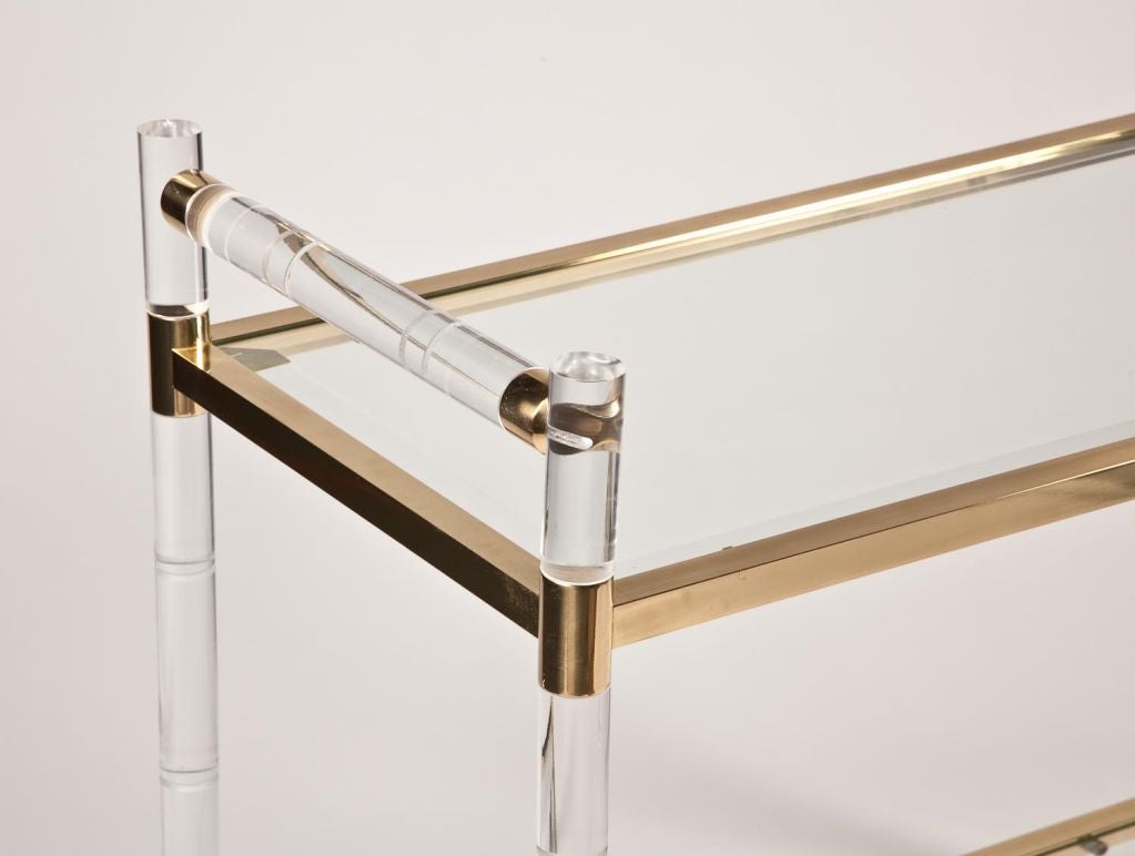 Midcentury glam stylized bamboo Lucite bar cart with a brass frame and glass shelves.