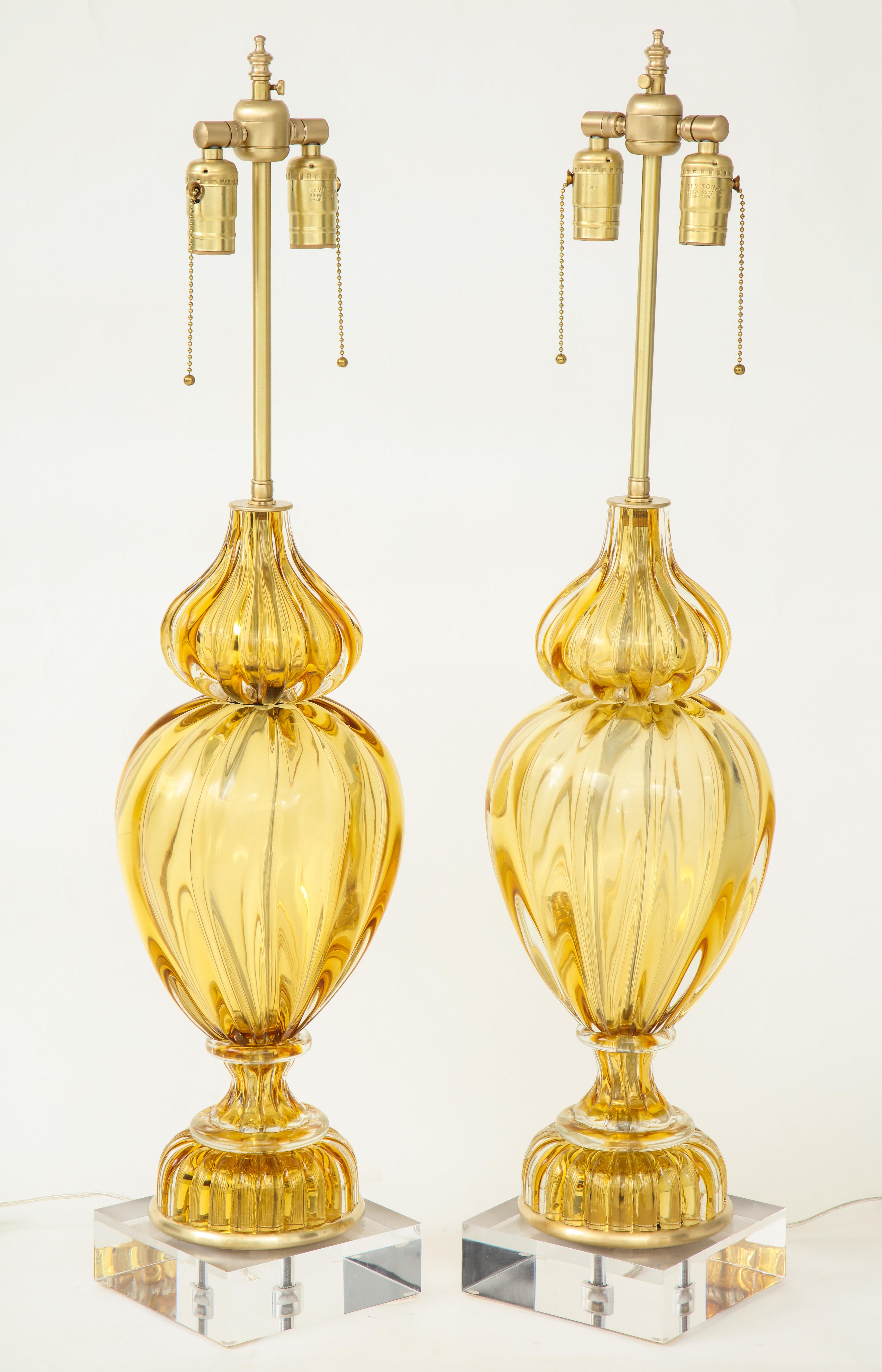 Striking pair of fluted Murano glass lamps in a light amber color with brass fittings sitting on custom Lucite bases. Rewired for use in the USA with brass double pull chain sockets. Seguso glass for Marbro.