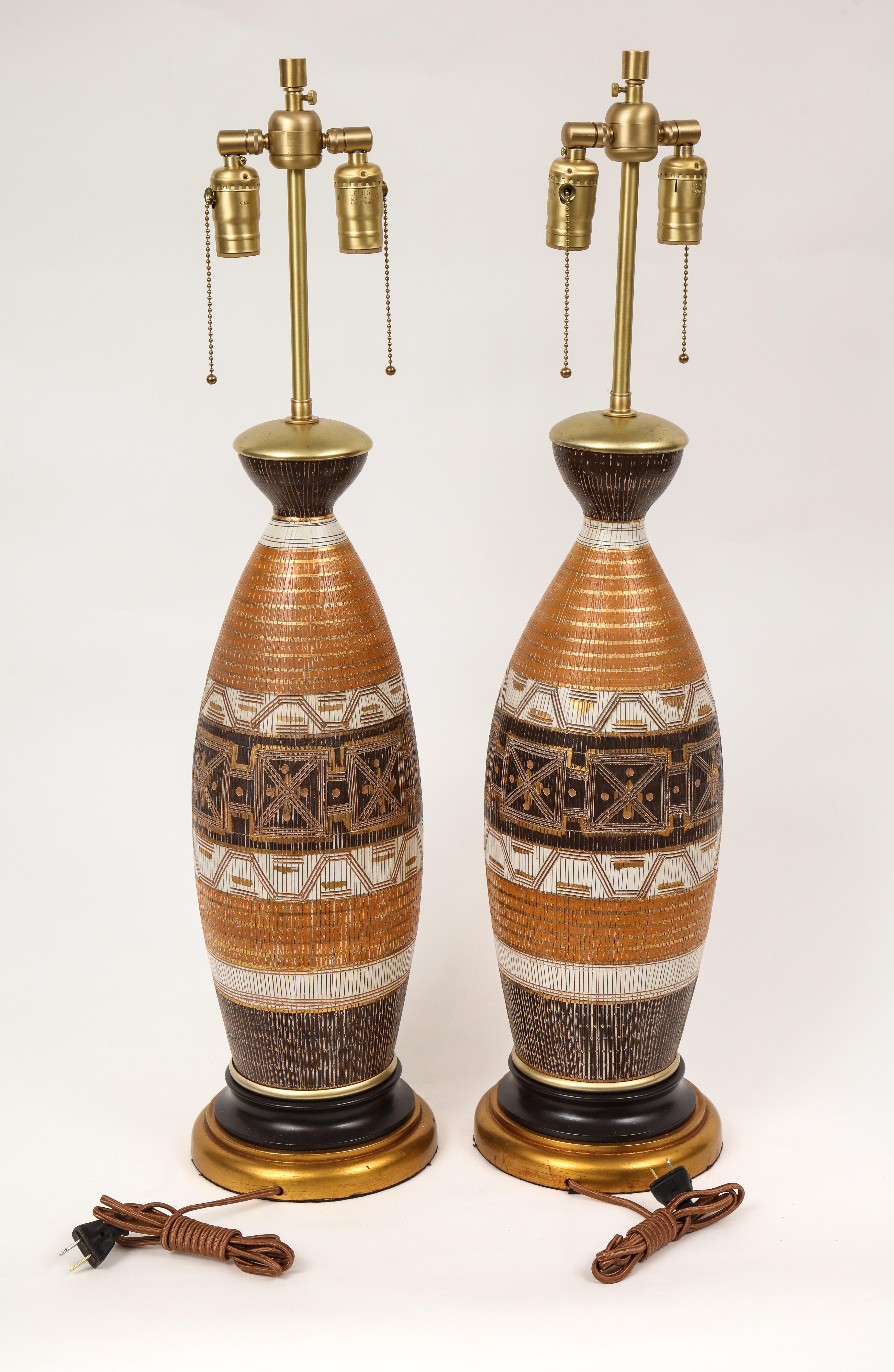 Midcentury Italian ceramic lamps featuring bands of brown, burnt orange, and off white with hand incised details and gilt accounts. Rewired for use in the USA with brass double cluster sockets.
Aldo Londi for Bitossi.