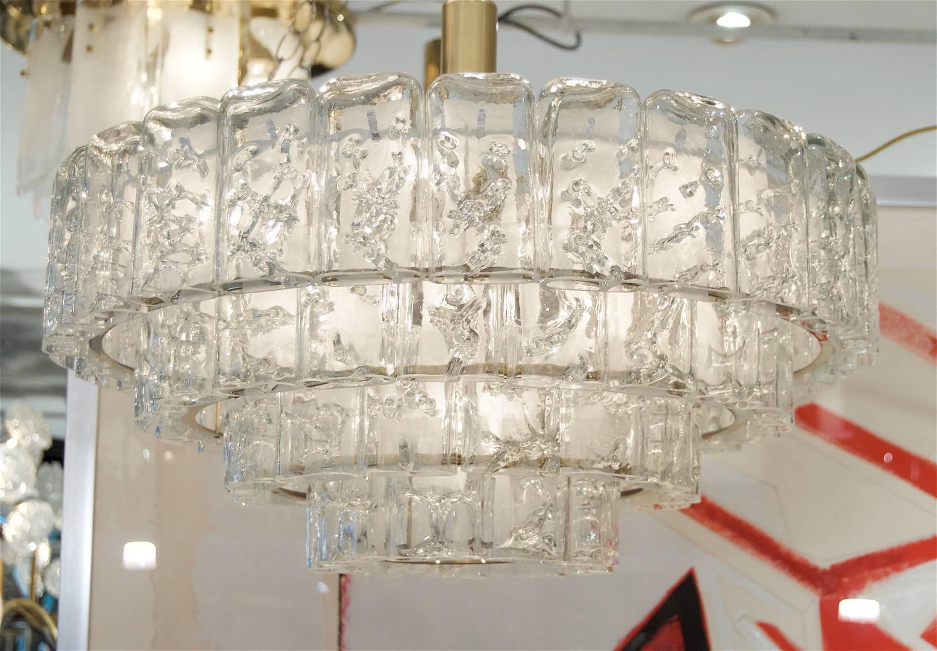 This fantastic and dramatic Doria chandelier is comprised of four tiers of individual glass pieces. The glass has the appearance of ice, each piece having internal random veining and a frosted reverse side. A thin brass ring ornaments the interior