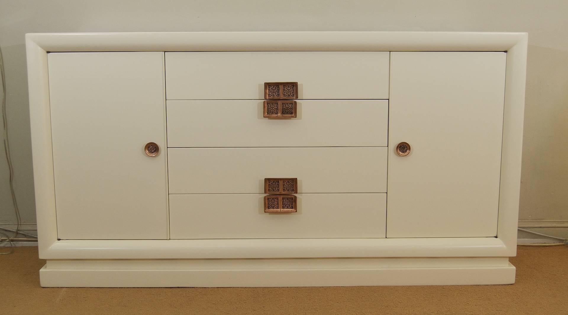 A large white lacquered dresser with intricate Asian inspired copper tone pulls. The dresser has four center drawers and two outer cabinets each with four interior drawers. Enough storage for the largest of wardrobes.