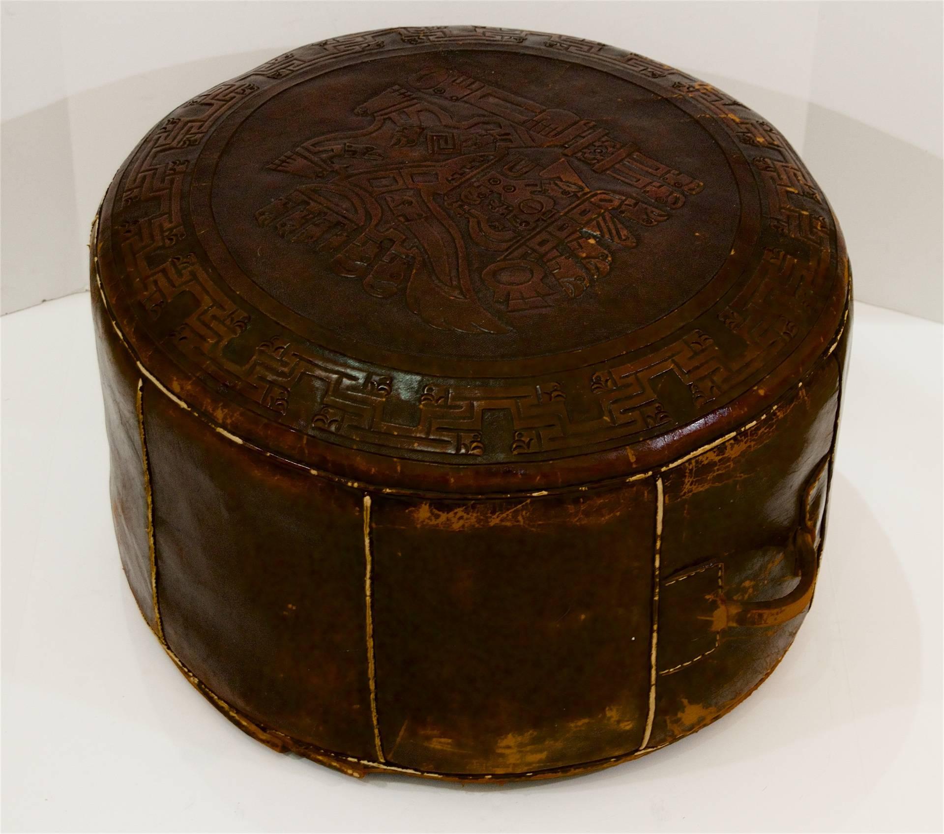 A brown leather pouf with embossed Aztec or Incan motifs. Perfect occasional seating or as an ottoman.