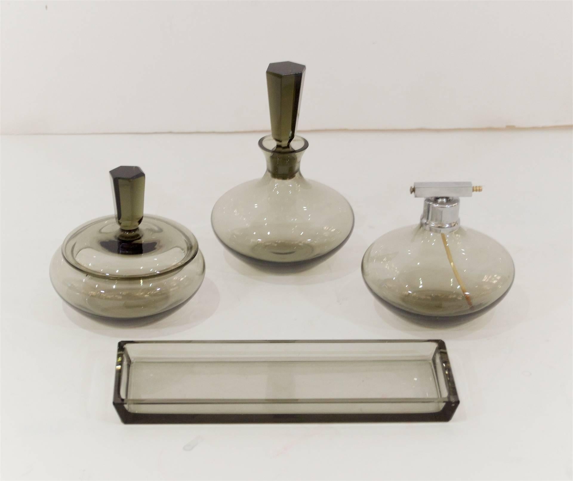 Art Deco smoke tone crystal vanity set. 

Includes perfume bottle, eau de cologne bottle, powder dish and trinket tray. 

Dimensions listed are of eau de cologne bottle.

Please note the perfume bottle is lacking atomizer bulb - due to the age