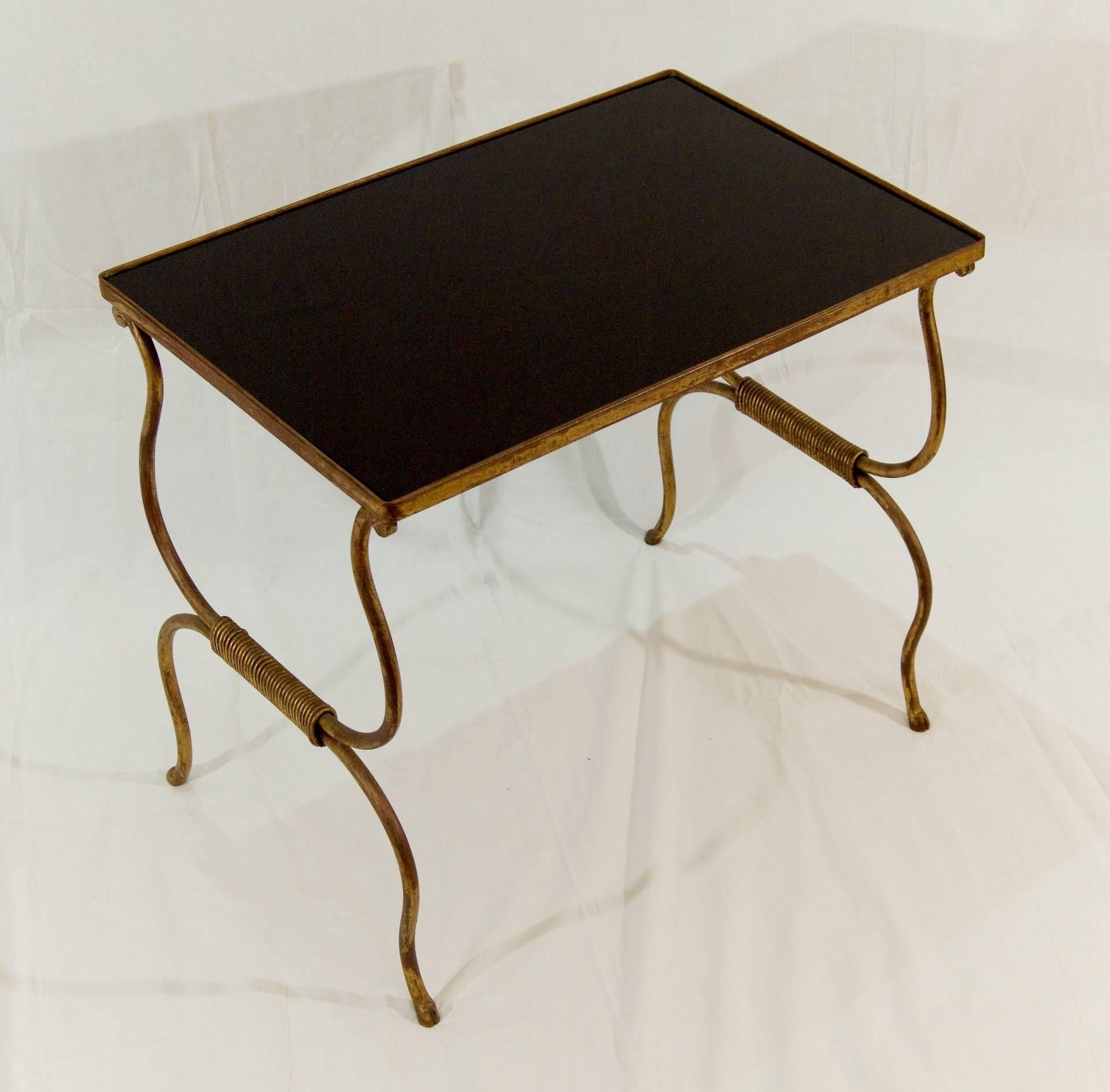 A gilt painted wrought iron table with nicely formed hoofs at the end of each leg. The top is black glass.
