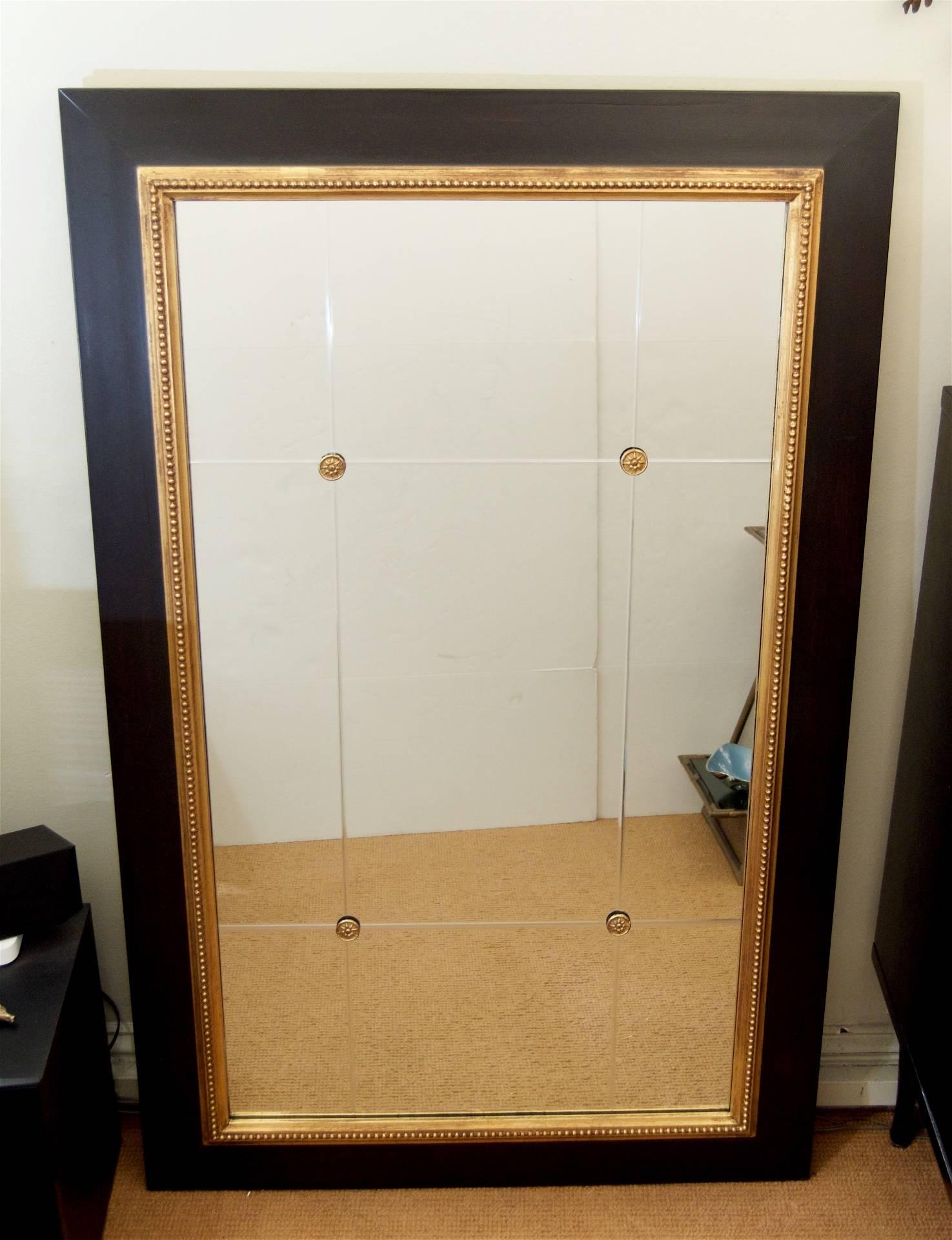 Elegant ebonized wood framed wall mirror with incised beveled detailing and gilt rosette accents.