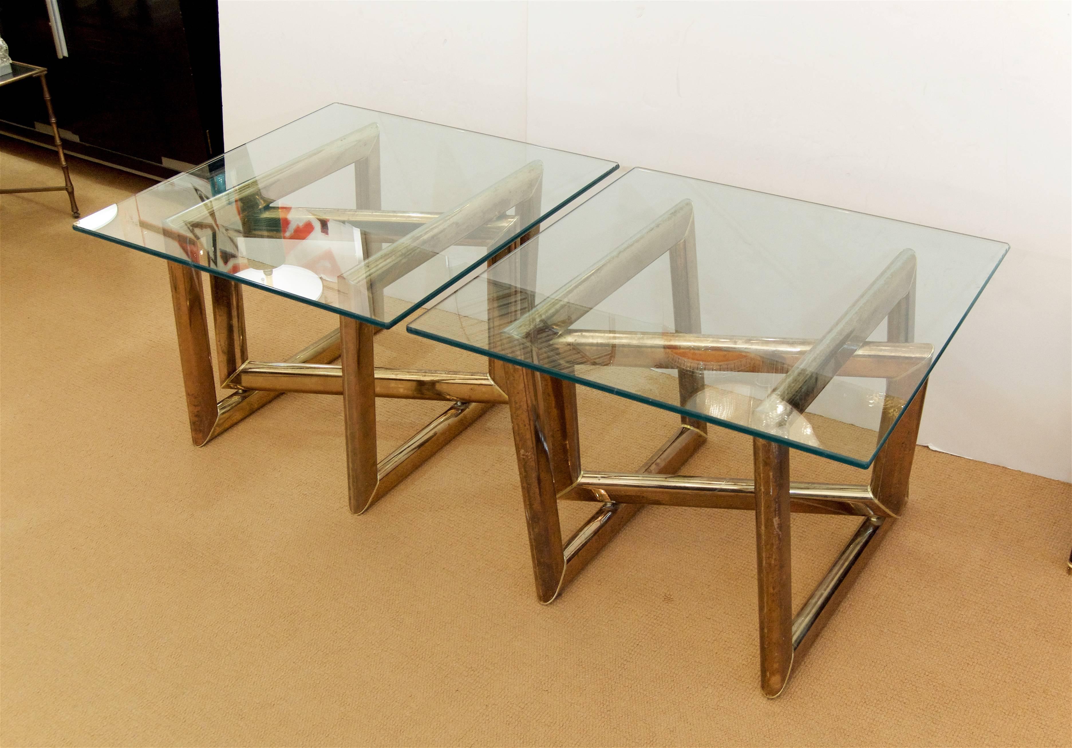 Pair of sculptural end tables comprised of three brass parallelograms oriented at unusual angles, creating an sense of imbalance while providing a substantial and impressive support to the square glass tops. Segments of brass are joined with thin