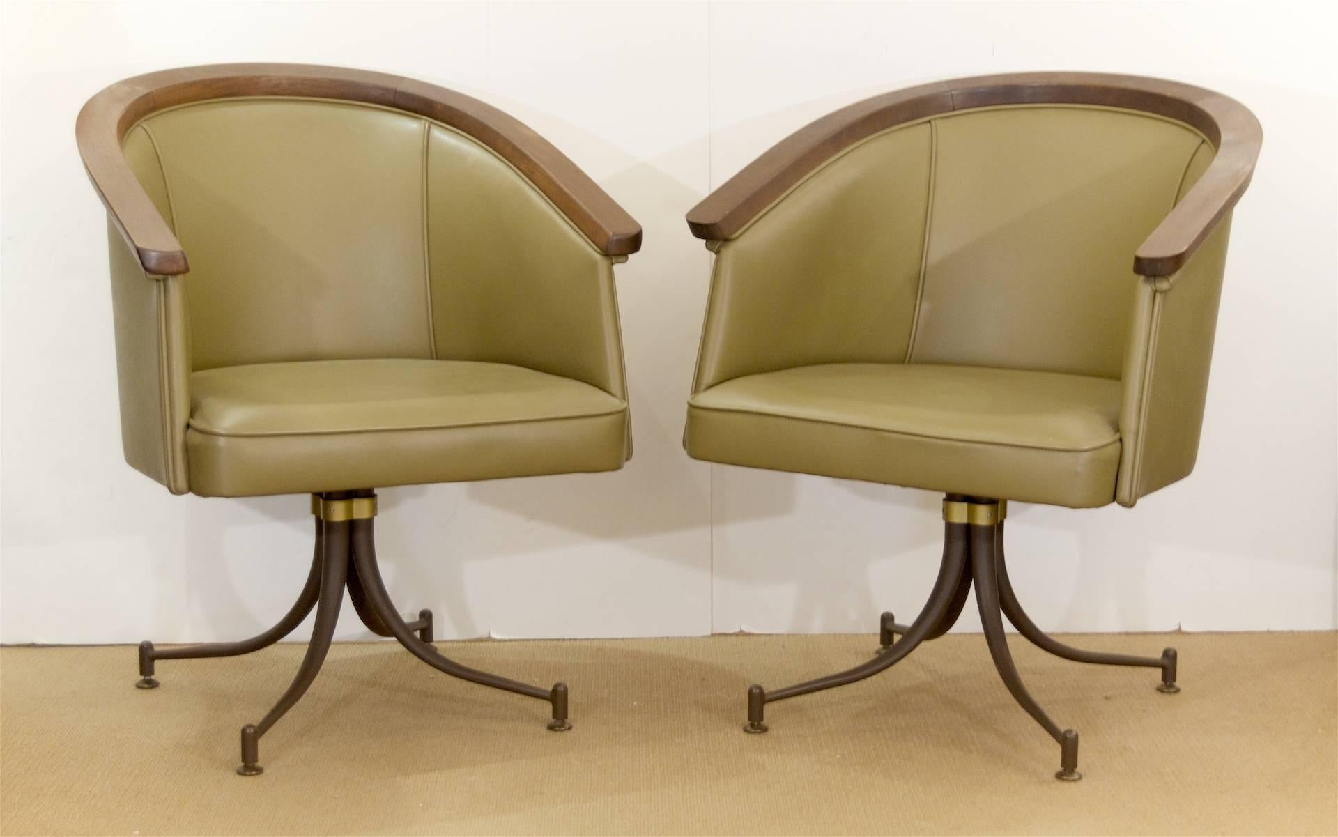 Pair of olive tone, vinyl-upholstered swivel base armchairs by Troy Sunshade Company - style reminiscent of earlier pieces designed by Gilbert Rohde for the company.

Elegant curved wood arm piece and brass detailing at the swivel base mount,