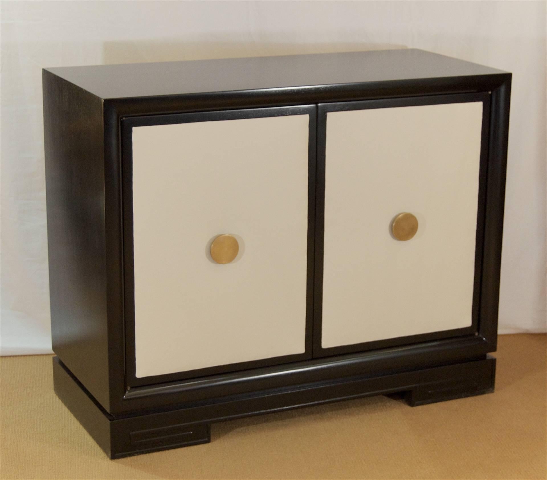 Gorgeous Hollywood Regency chest of drawers in satin black lacquer. The cabinet doors are covered in a cream leather with large, original circular brass pulls. The base of the piece has a subtle Greek key accent. Five interior drawers for a