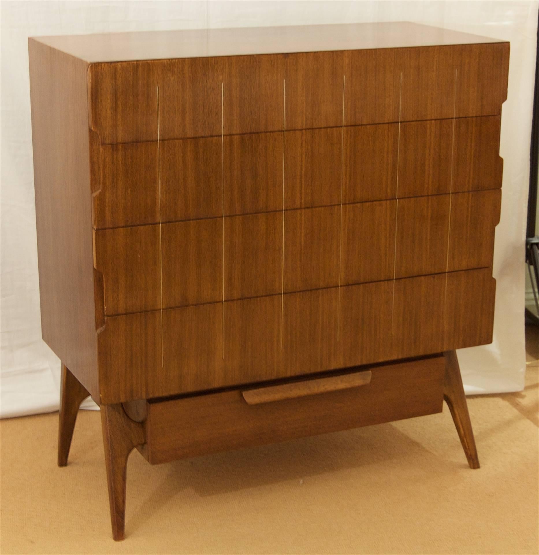 Gorgeous walnut chest of drawers with brass inlay detailing on a splay leg base.
Each drawer has a cut-out detailing on the edges which serves as drawer handles, giving this piece interesting lines.

The lowest drawer features a cedar bottom for