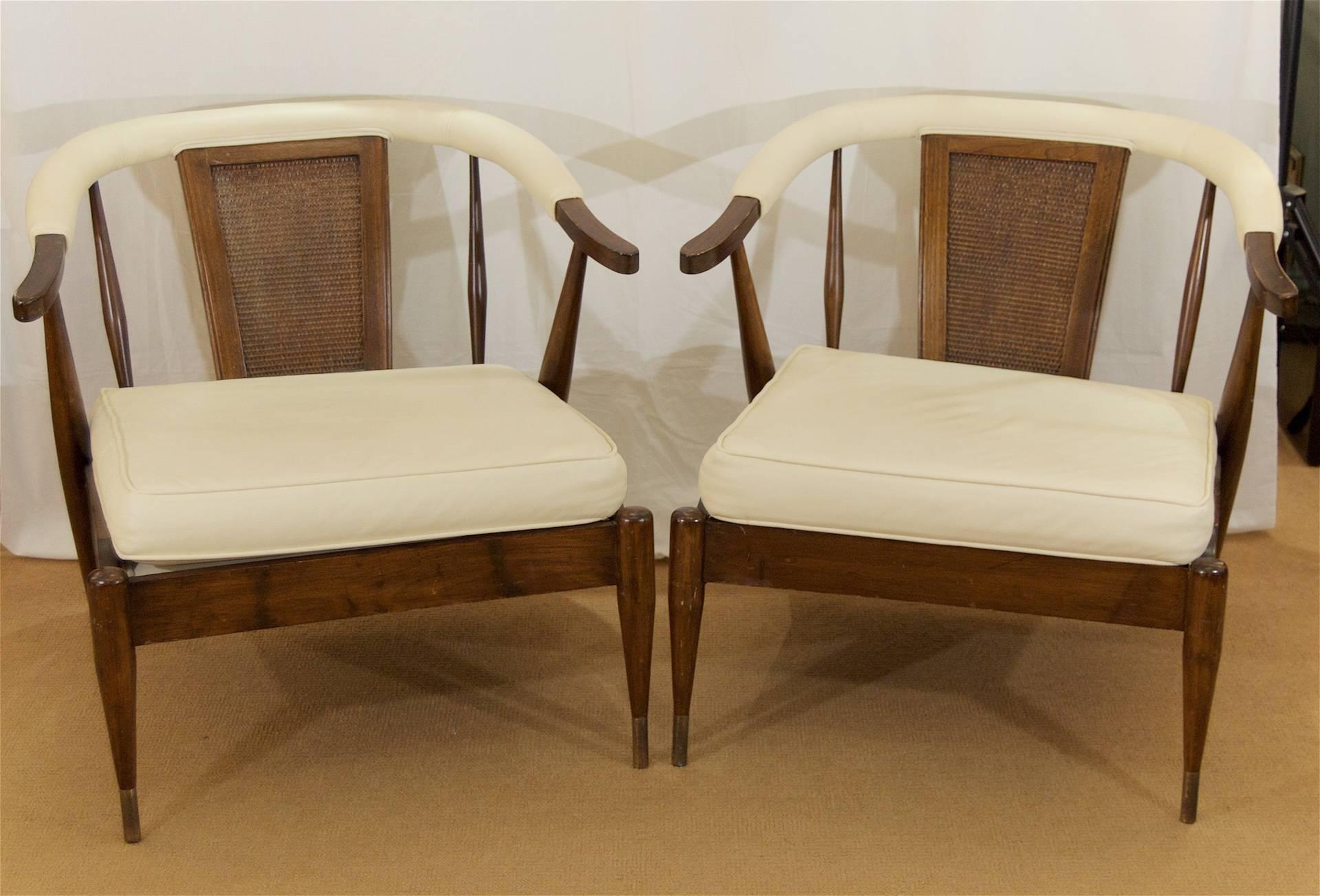 An excellent pair of well-proportioned lounge chairs with low-slung seats, the yoke-form walnut frames retaining their original finish. Brass sabot on front legs with age-appropriate patina. Upholstery is recent, in soft high-end faux cream leather.