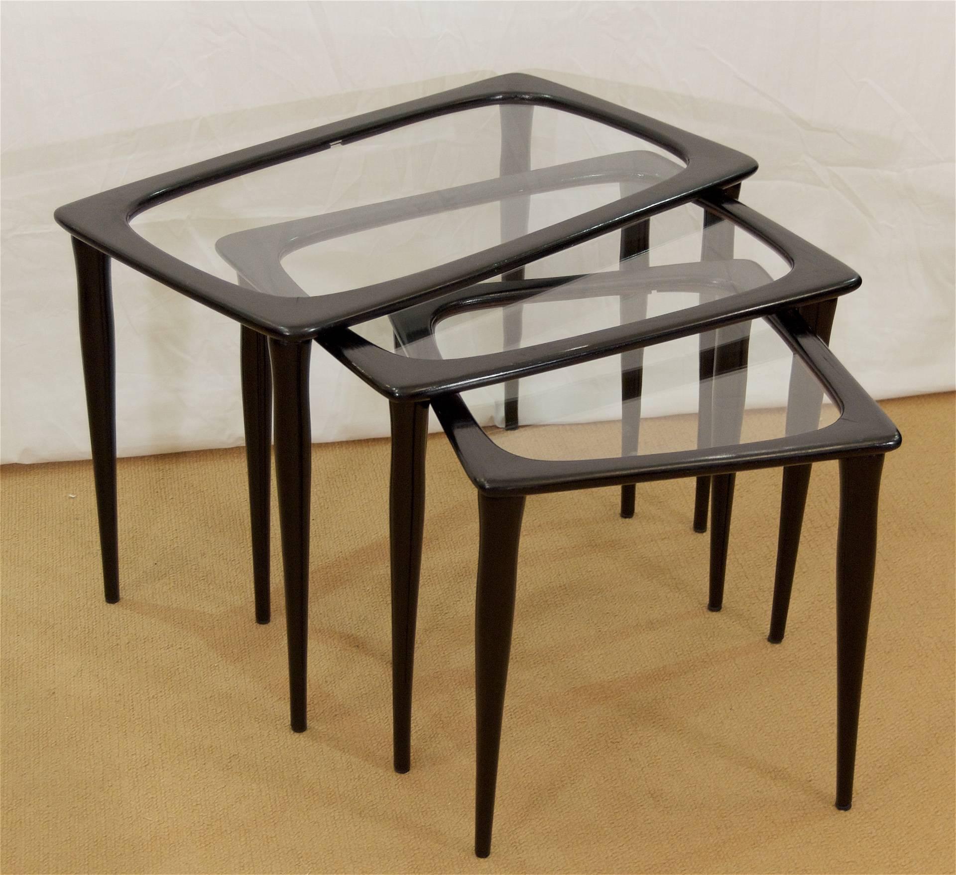 Excellently shaped set of three nesting tables in ebonized wood with glass centers and a gently curved structure to the wood frames, similar to Ico Parisi style. Dimensions given are of largest. Measure: Medium table measures 20.25 x 14.75 x